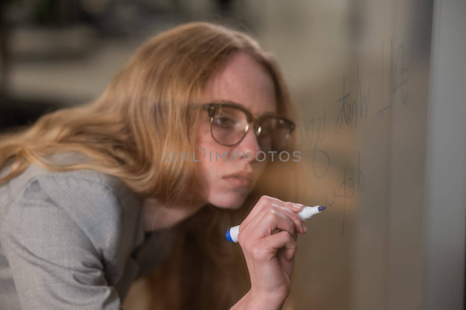 Caucasian woman with glasses writes text in English on a glass wall. by mrwed54