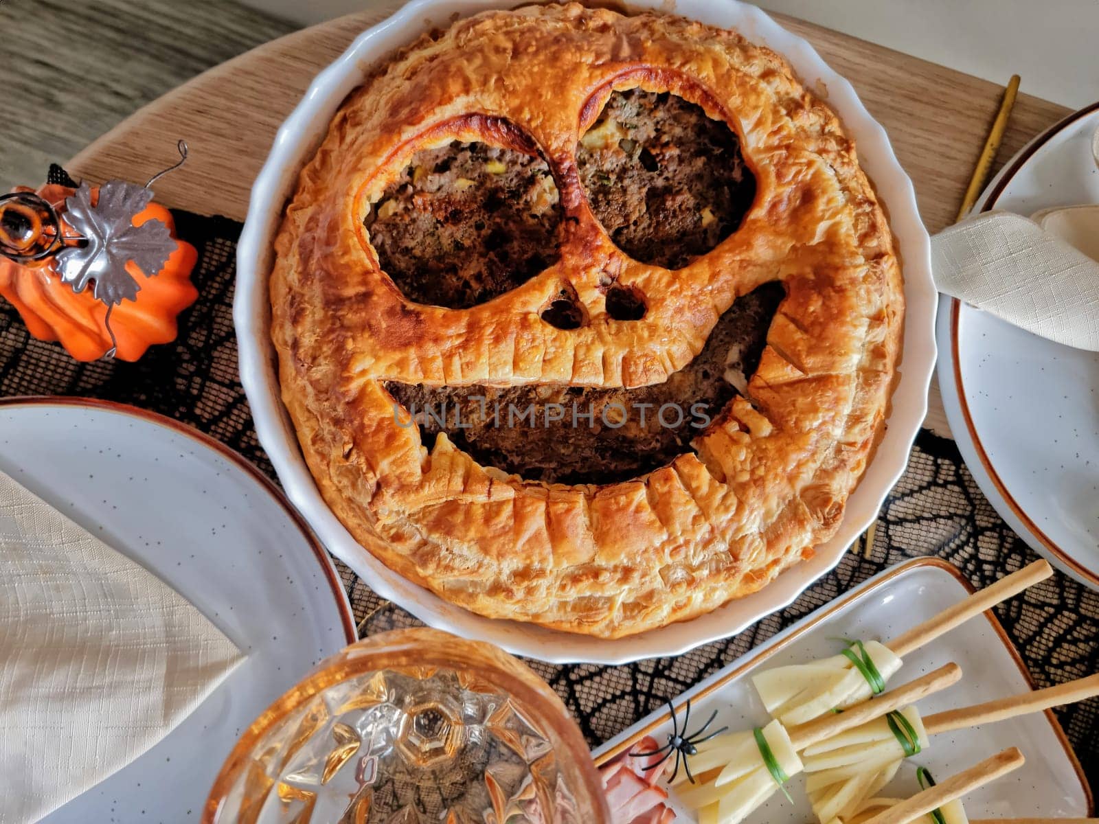 table setting for a Halloween party. Appetizing, rosy, baked meat pie in the shape of Jack O'Lantern by Leoschka