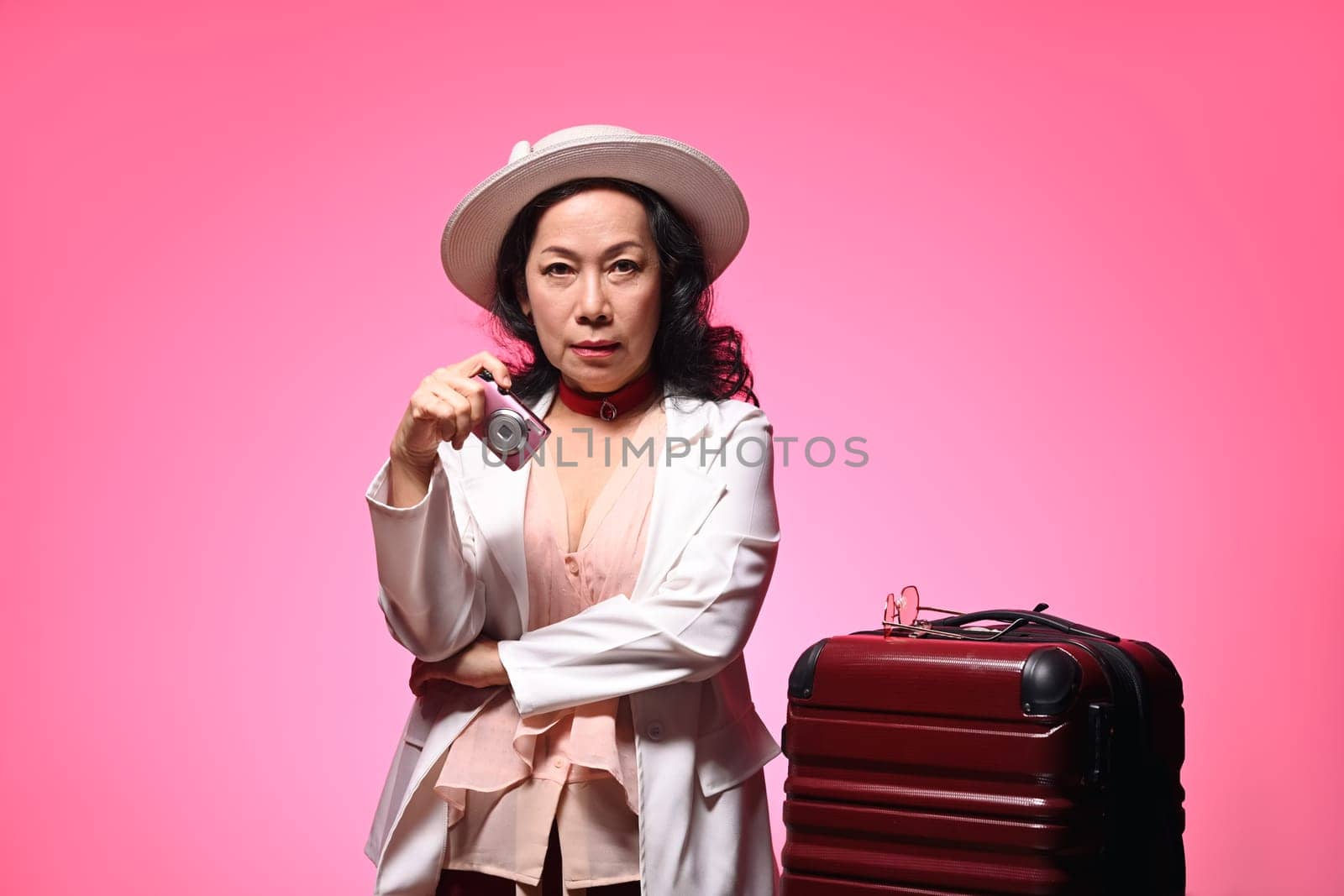 Senior woman with travel accessories on pink background. Summer, travel and vacation concept.