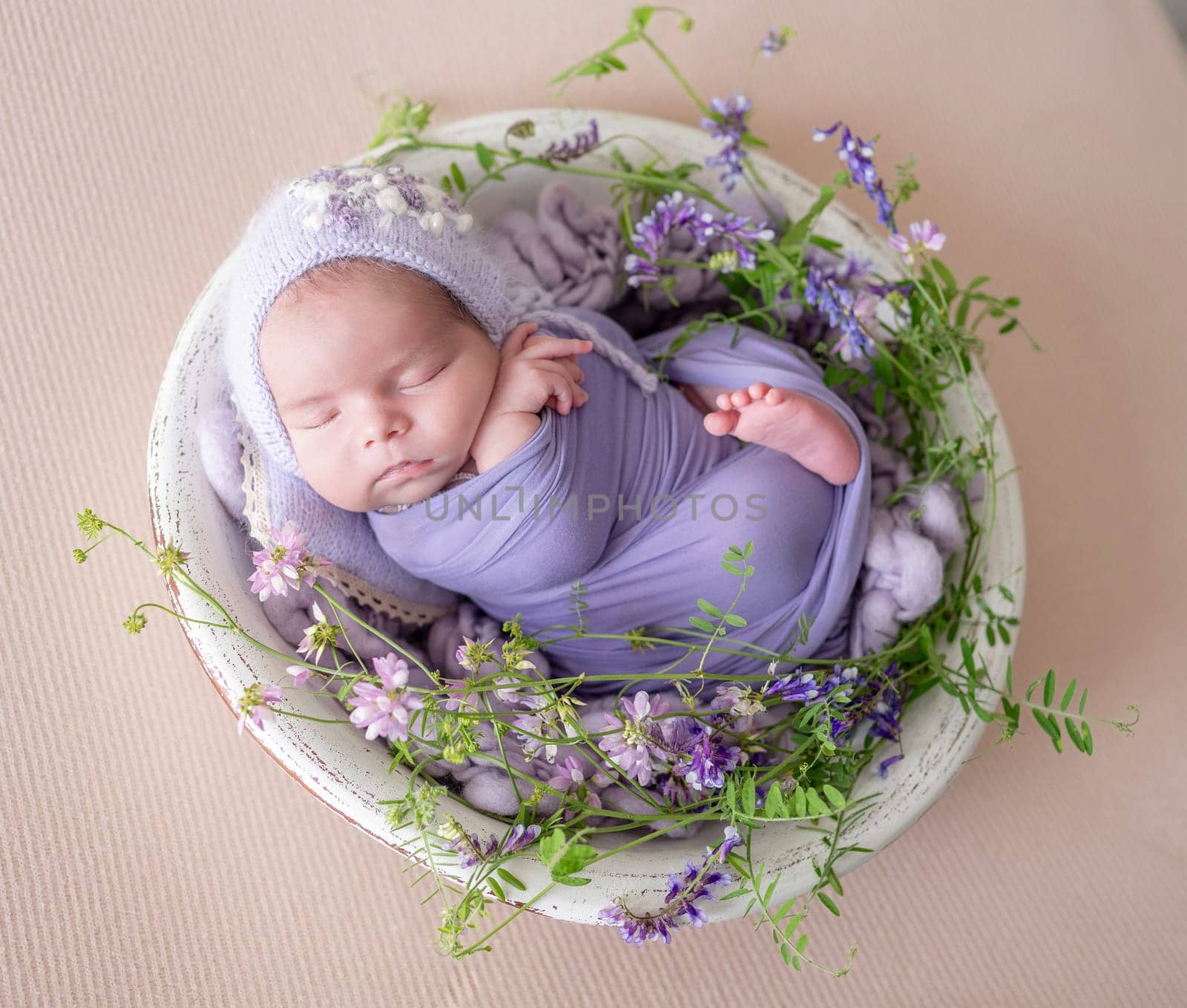 Newborn Baby Girl Sleeps In Basket With Flowers During Studio Photoshoot