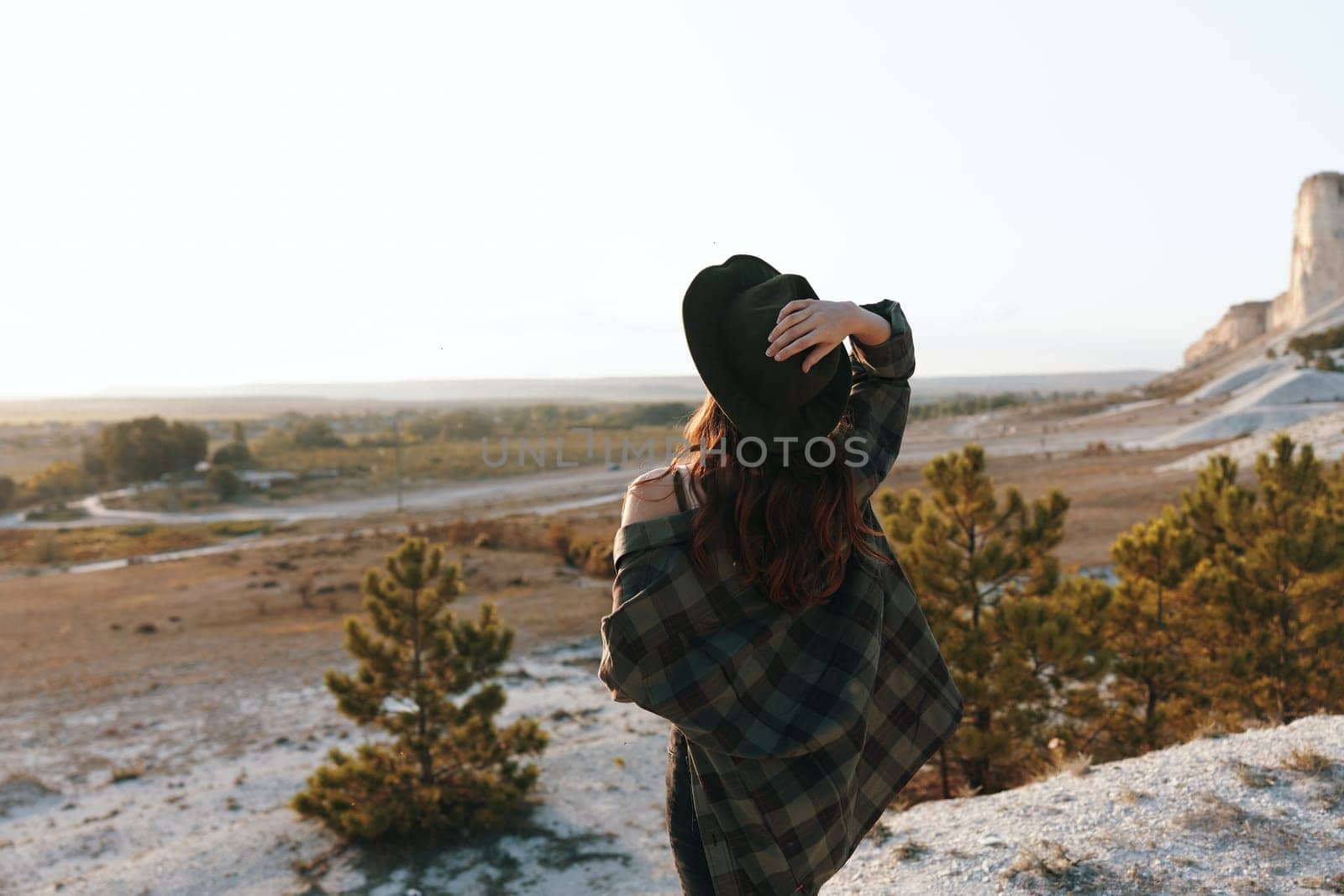 serene woman in plaid shirt and hat gazing at sunset over majestic mountains by Vichizh