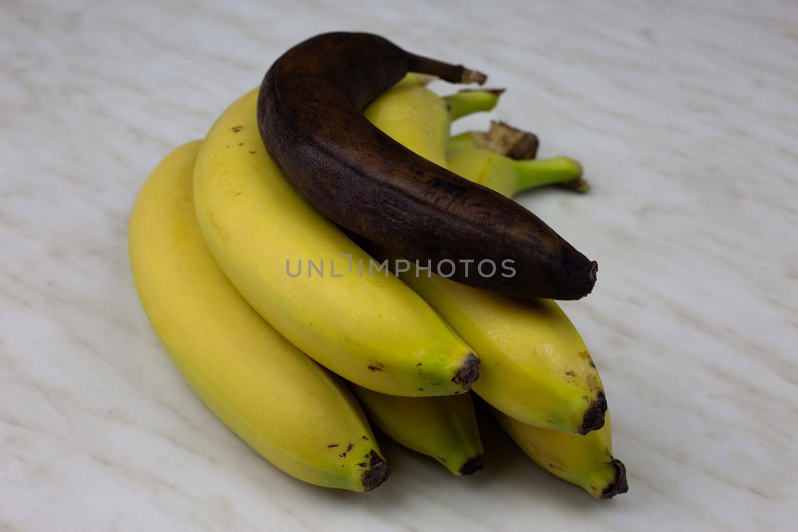 Bunch of bananas with one rotten banana. Overripe spoiled banana not suitable for eating lies on fresh juicy banana fruit, unhealthy eating with healthy food