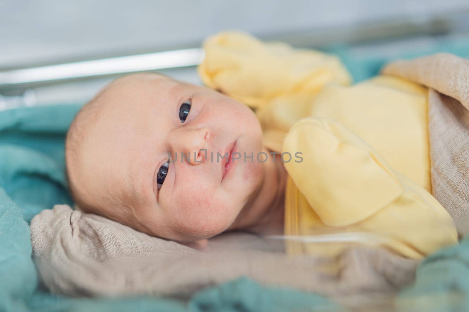 A newborn rests peacefully in his transparent bassinet in the hospital. The clear bassinet provides visibility for medical staff to monitor the baby's well-being while ensuring a safe and comfortable environment for the newborn.