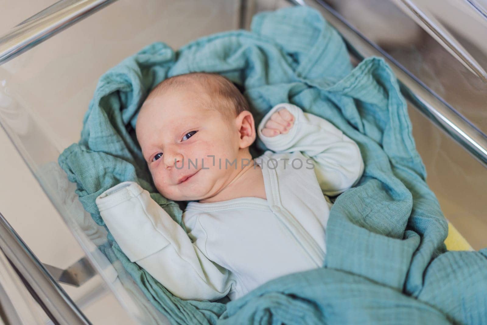 A newborn rests peacefully in his transparent bassinet in the hospital. The clear bassinet provides visibility for medical staff to monitor the baby's well-being while ensuring a safe and comfortable environment for the newborn.