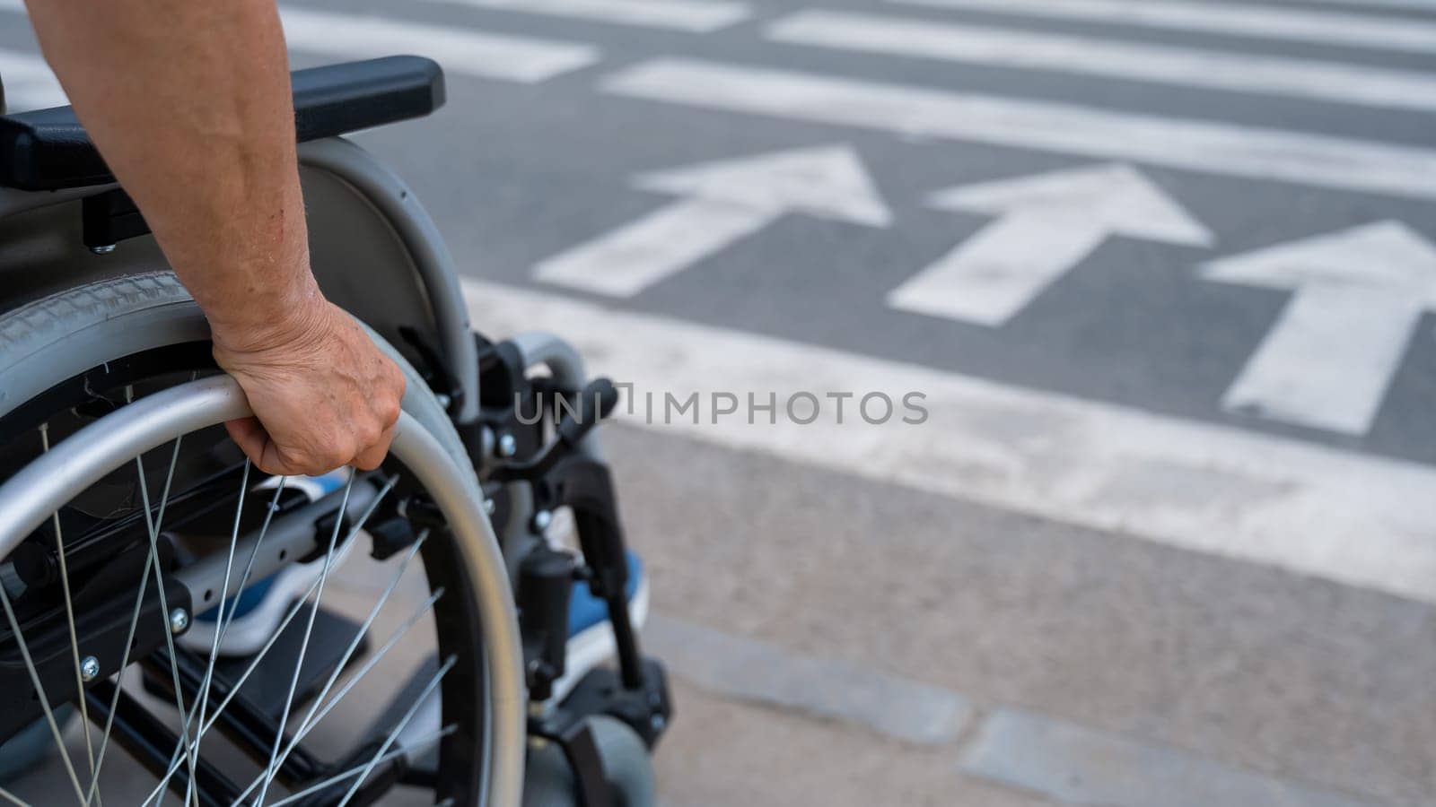 Rear view of an elderly woman in a wheelchair going to a pedestrian crossing. Close-up on wheels