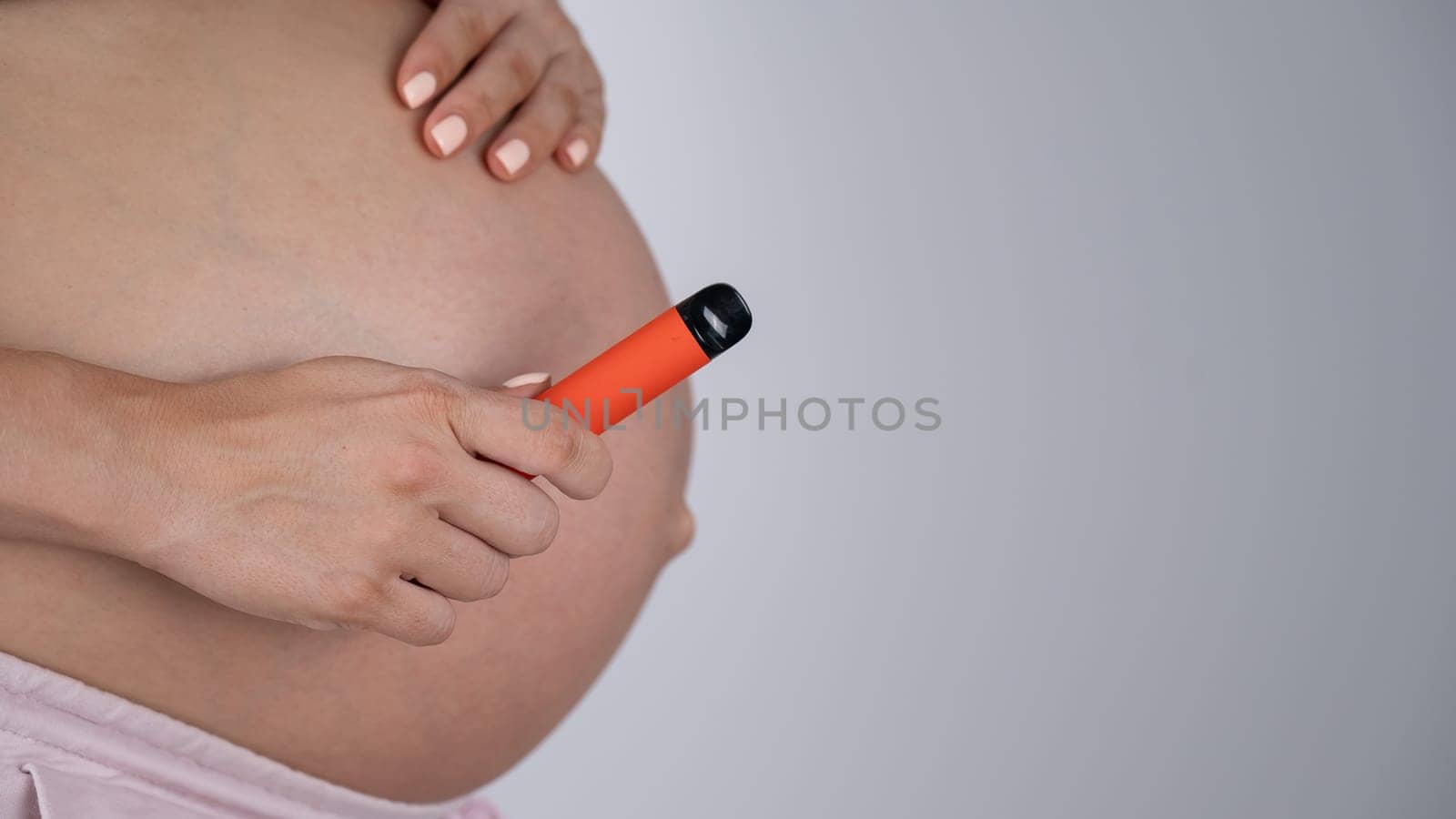 A pregnant woman smokes a vape. A girl holds an electronic cigarette against the background of her bare tummy. Copy space