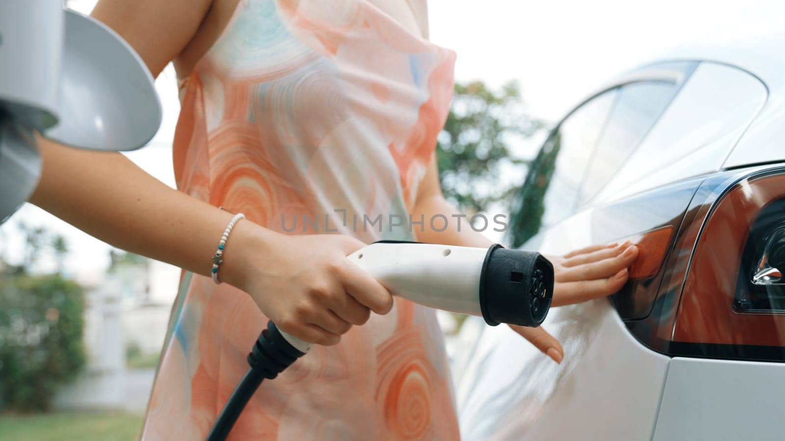 Closeup woman recharge EV electric car's battery at parking lot in natural green park. Clean energy technology for rechargeable vehicle for sustainable and eco friendly travel. Synchronos