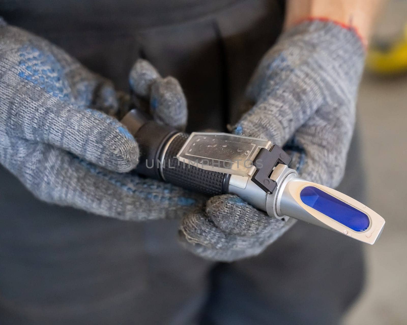 A mechanic holds a Refractometer in a car service center. Portable optical device for determining the freezing point of antifreeze