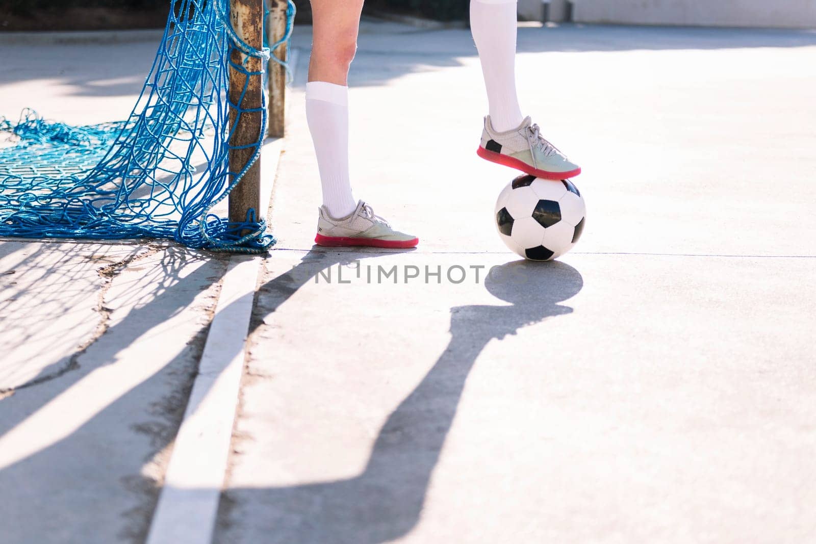 close up of the feet of a female football player stepping on a soccer ball next to the goal of an urban court, concept of sport and active lifestyle, copy space for text