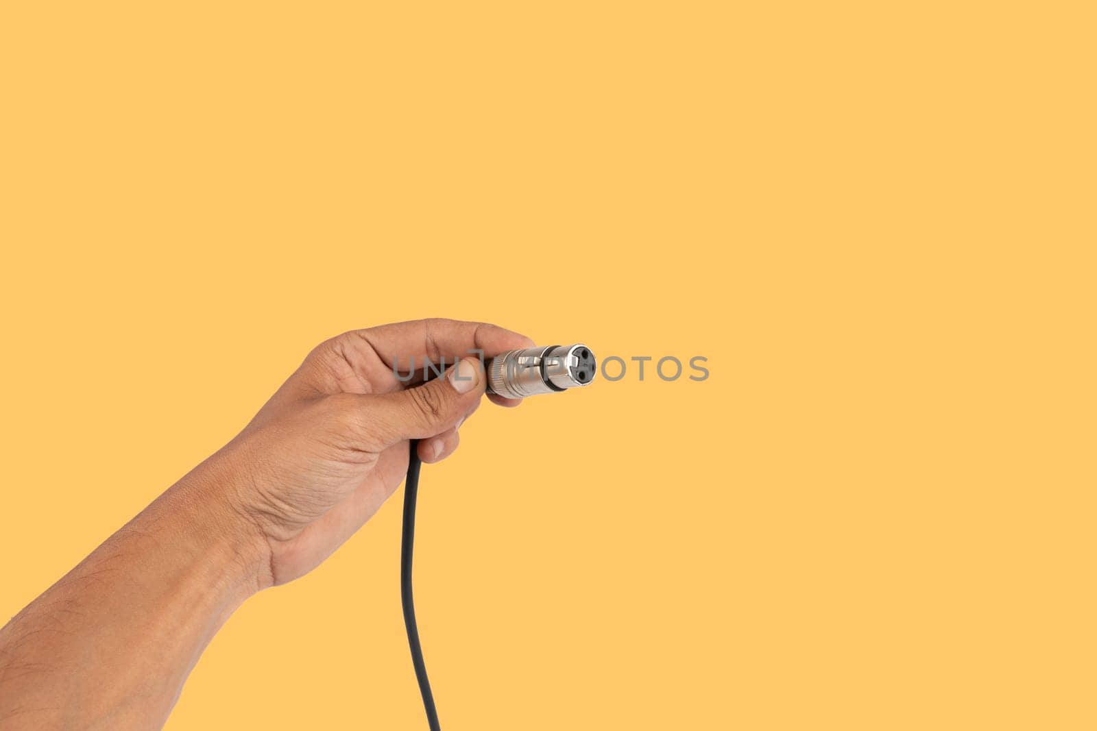 Male hand holding an XLR audio connector cable isolated on yellow background. High quality photo