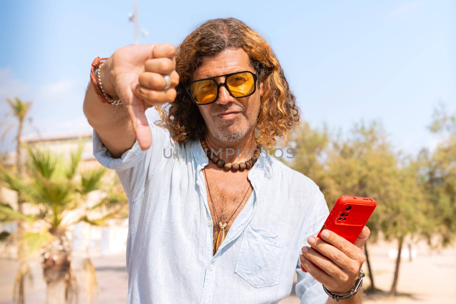 Caucasian man wearing sunglasses feeling serious showing his finger down in disapproval outdoors.