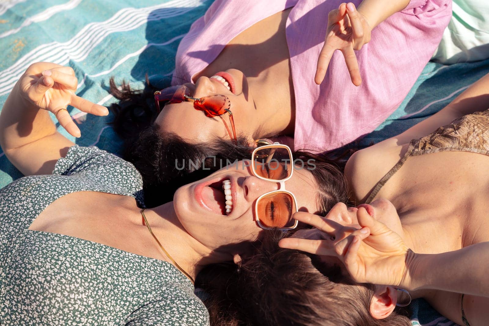 Three young women sunbathing on beach towels on the sand by molesjuny