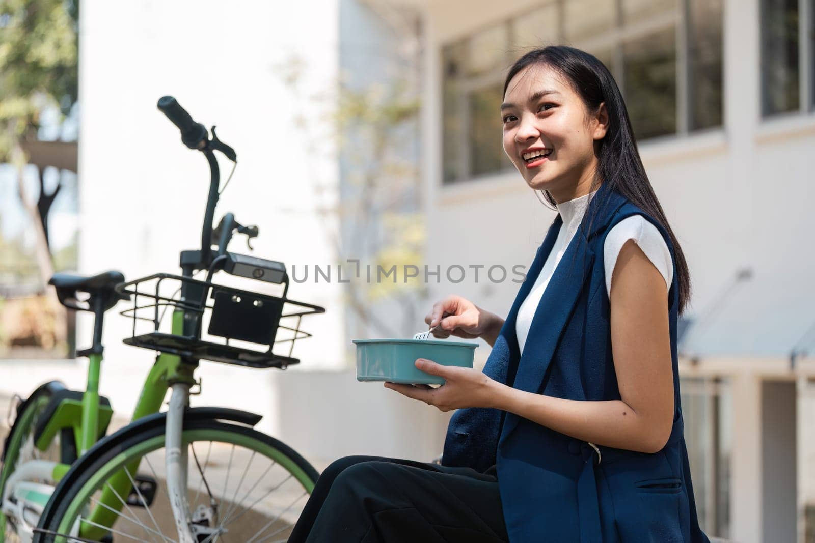 A young professional enjoying an eco-friendly lifestyle, featuring a bicycle and reusable lunch container in a modern urban environment.