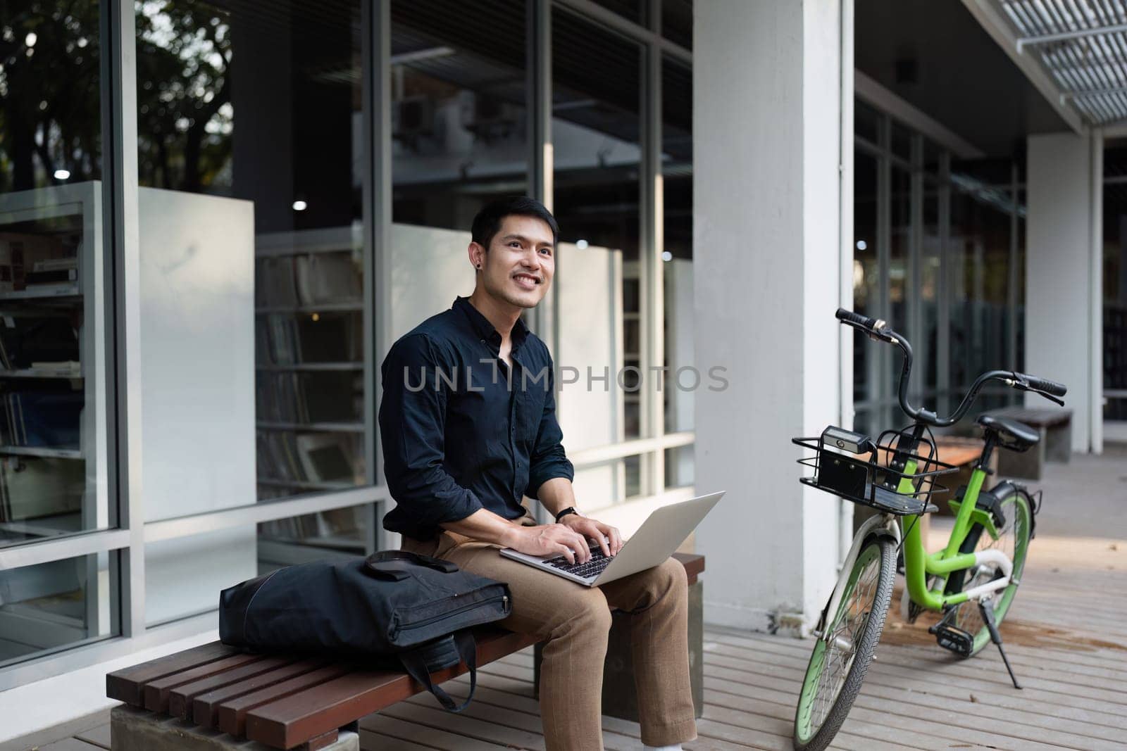 Young professional working on a laptop outdoors, promoting an eco-friendly business lifestyle with a bicycle and modern office setting.