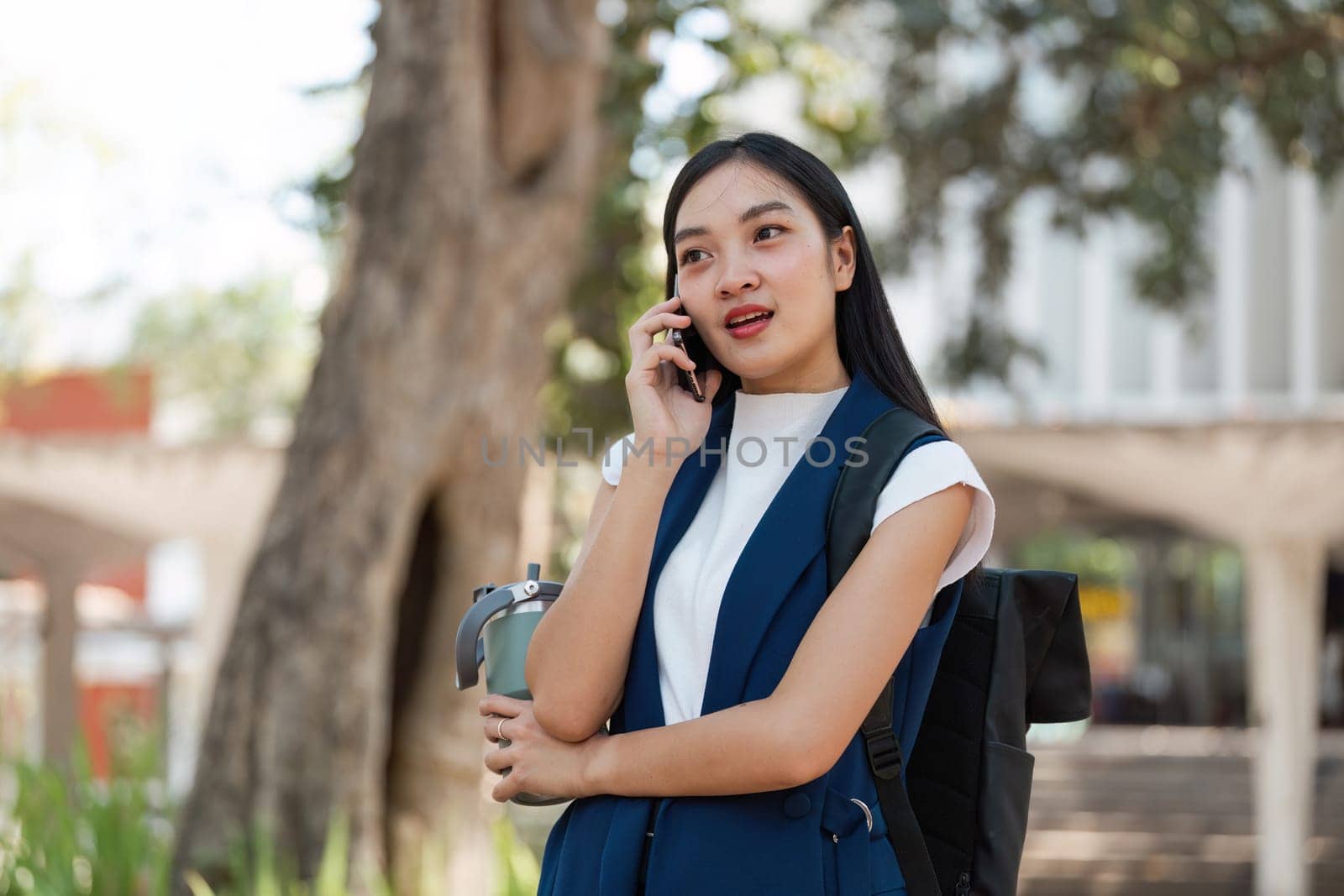 Young professional woman in sustainable fashion, talking outdoors on the phone, embodying modern eco-friendly business practices in an urban green environment.