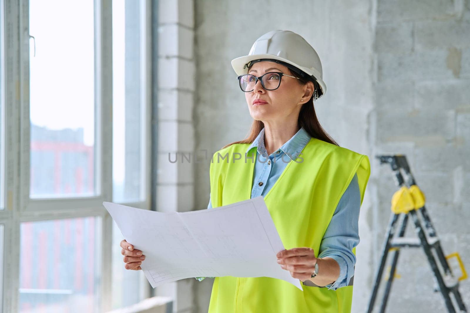 Technical profession woman in protective vest helmet working on construction. Confident serious industrial female engineer builder inspector supervisor architect with papers. Construction industry