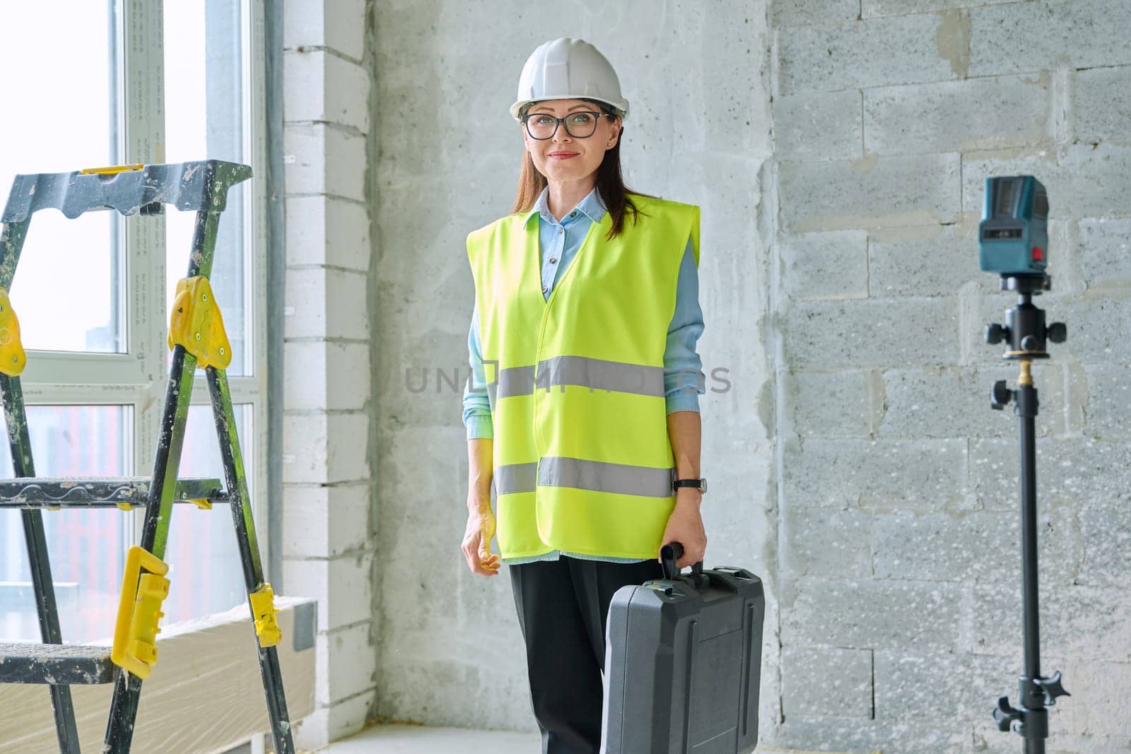 Portrait of woman industrial worker builder engineer architect supervisor at construction. Confident female in vest helmet with bag of equipment looking at camera. Construction technical professions