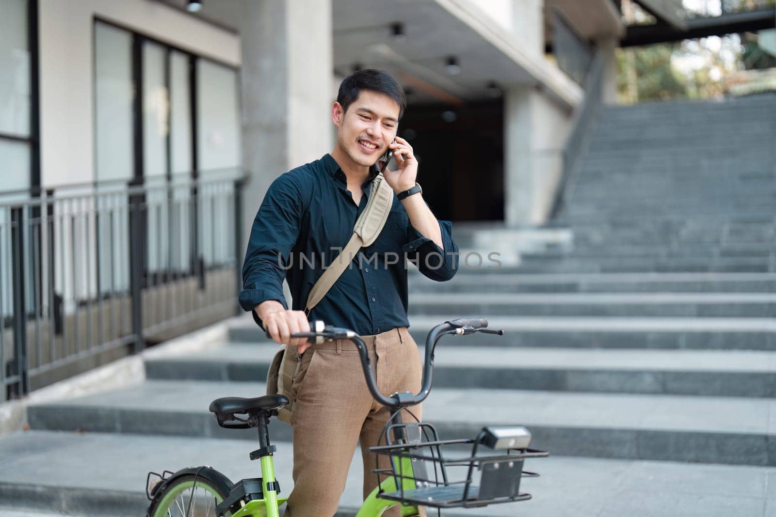 A young professional using a bicycle for eco-friendly commuting while talking on a smartphone in a modern urban environment.