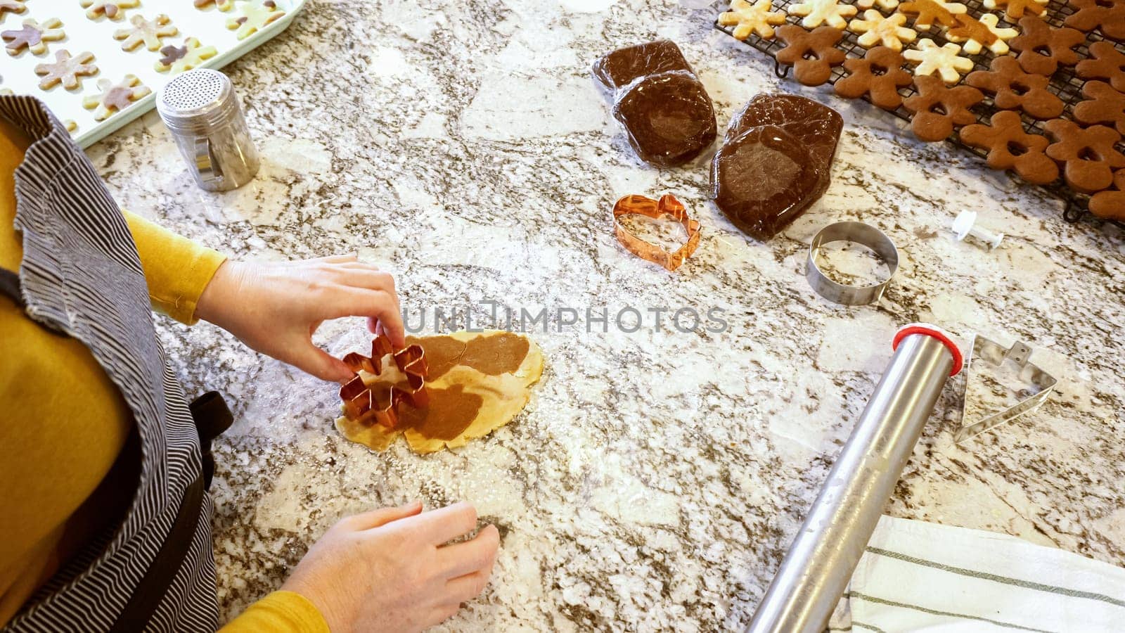 Using various festive cookie cutters, we're cutting out charming gingerbread cookies from the rolled dough on the sleek marble counter, bringing holiday cheer to the modern kitchen.