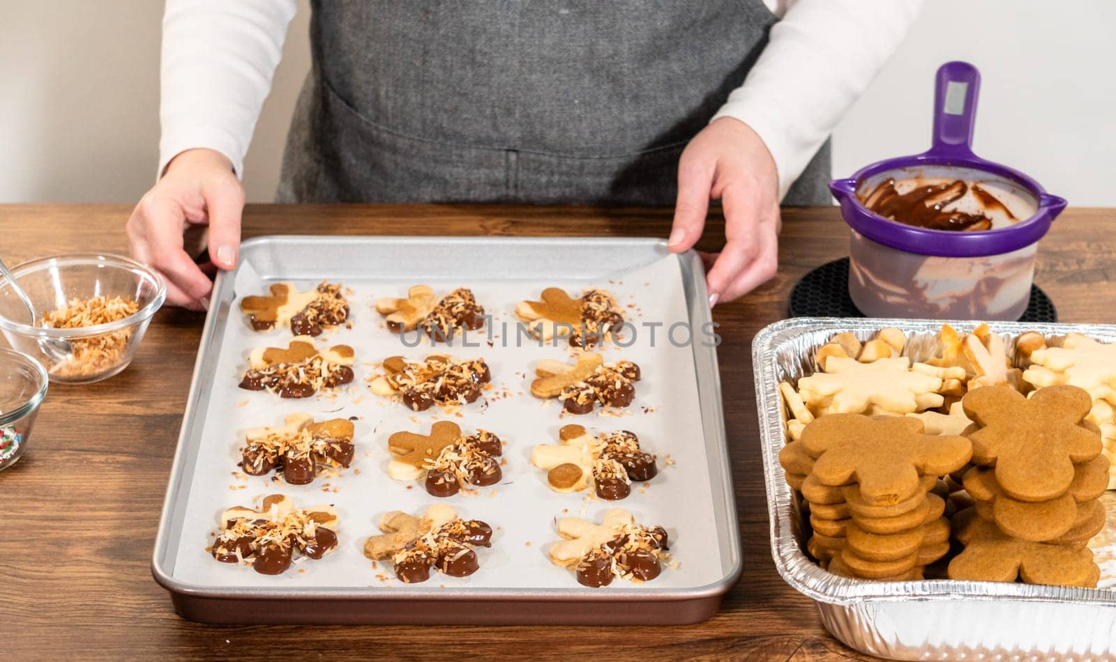 Gingerbread men cookies, chocolate-dipped feet, generously sprinkled with golden toasted coconut shavings, artfully arranged on parchment paper.