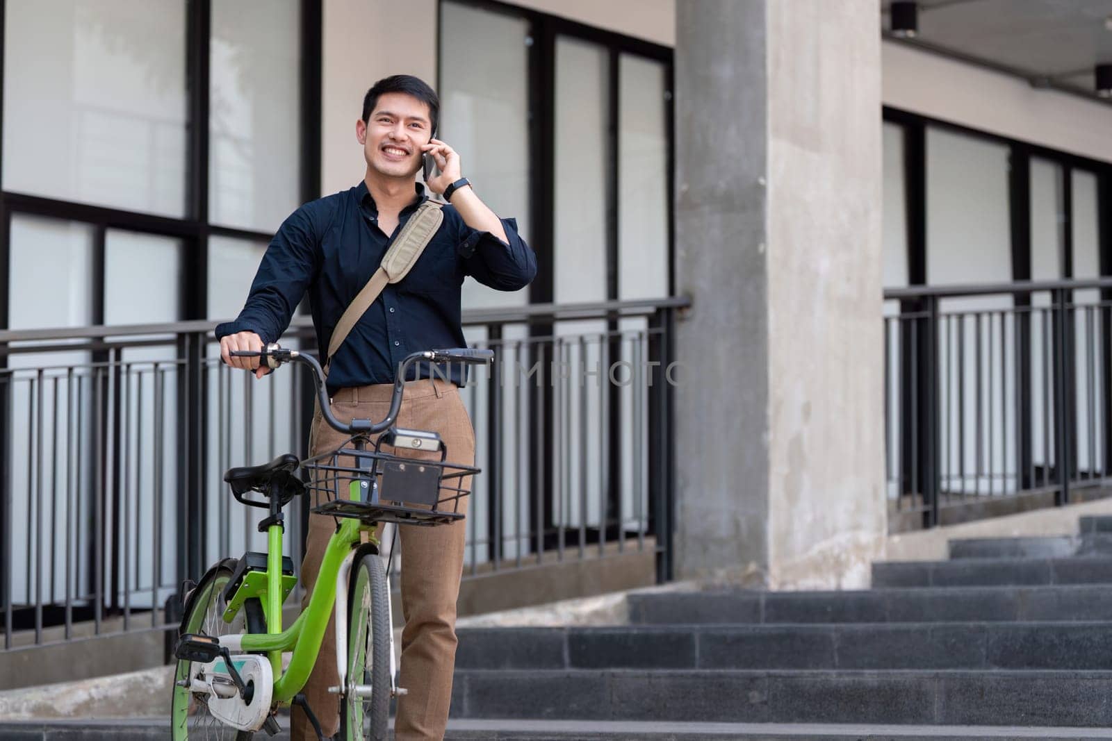 Businessman using a bicycle for eco-friendly commuting, talking on the phone, and working outdoors in a modern urban setting.