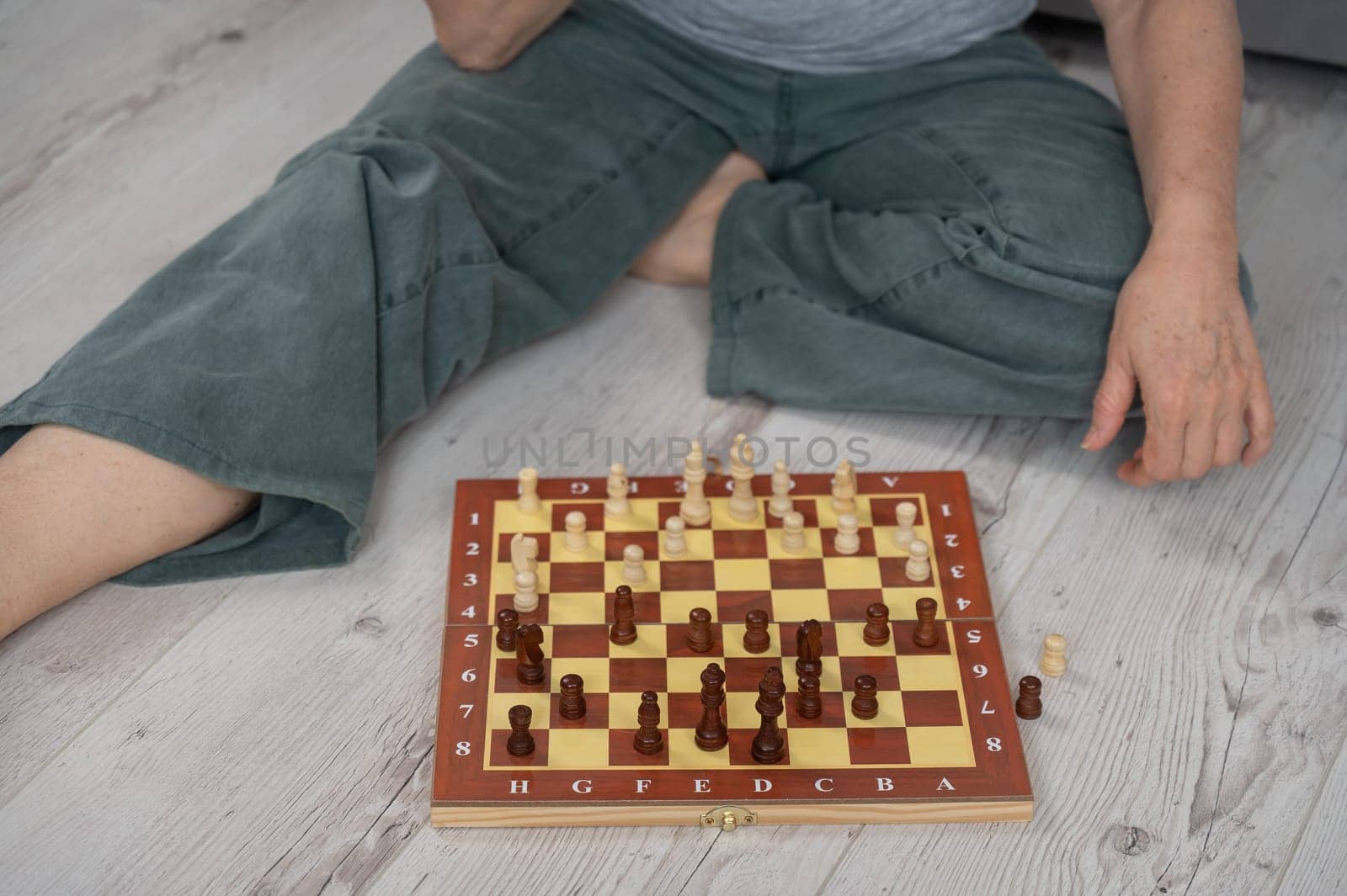 Faceless mature Caucasian woman plays chess while sitting on the floor.