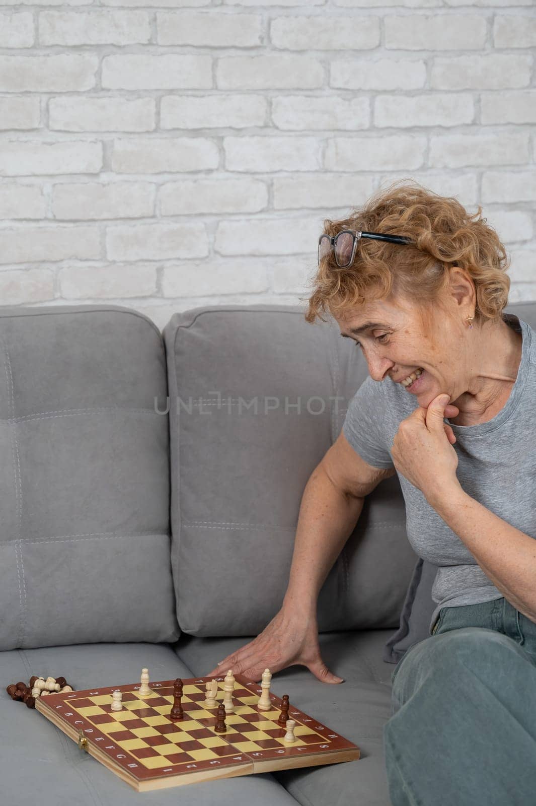 Mature Caucasian woman plays chess while sitting on the sofa. Vertical photo