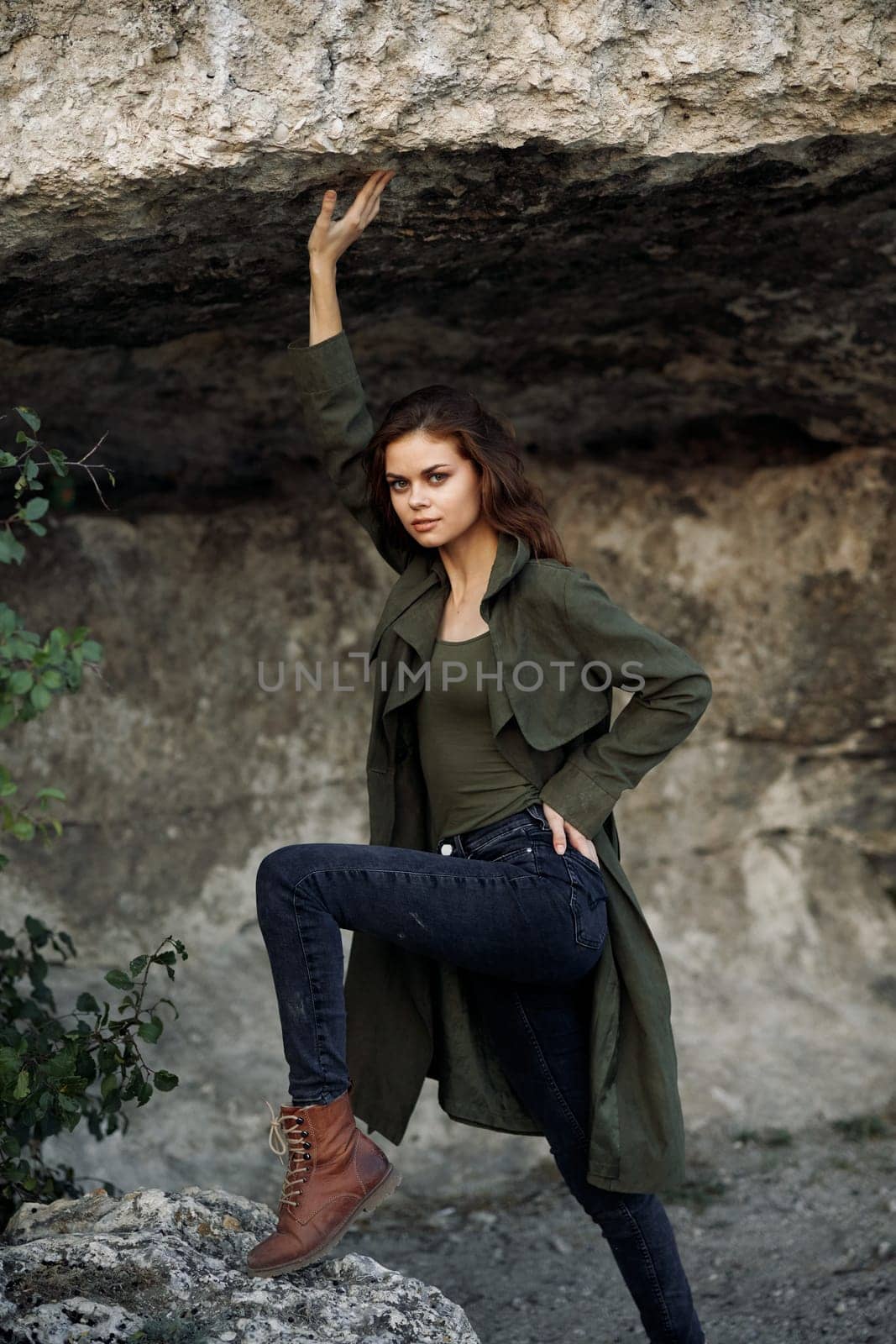 Woman in green coat leaning against rock in serene forest setting