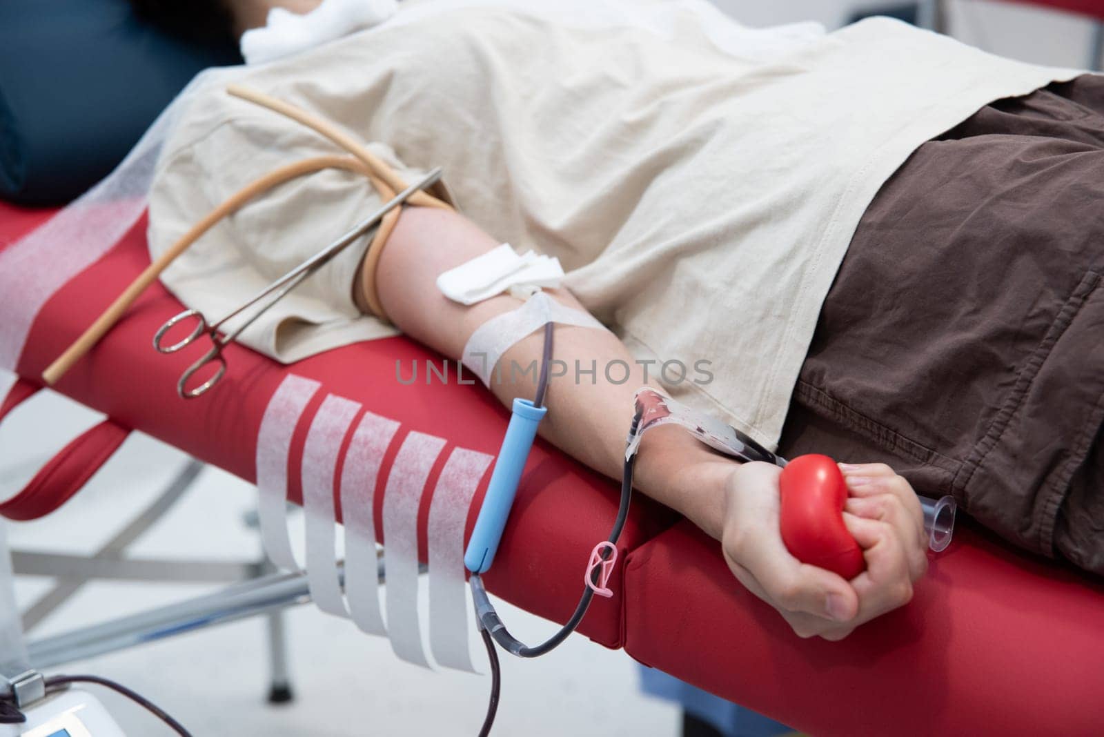 Hand of unrecognizable blood donor squeezing red heart-shaped rubber toy during transfusion process by Ashtray25