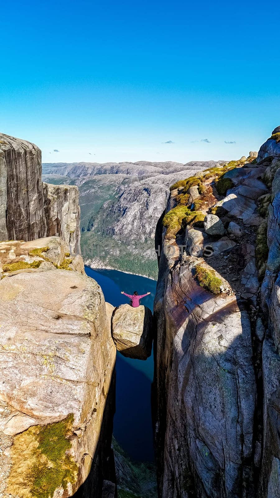 A person stands on the edge of the Kjeragbolten Pulpit Rock in Norway by fokkebok