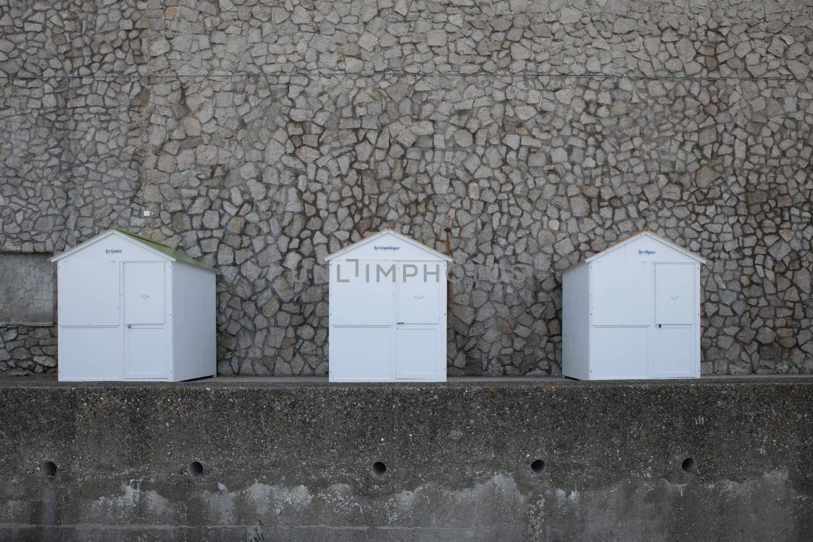 three white wooden beachhouses on the coastline of etretat in normandy in france with walls from rocks