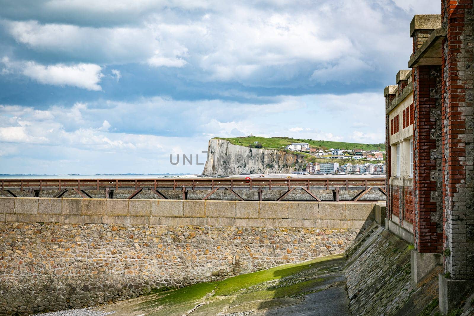 old wooden bridge and lighthouse in the harbor of the french vilage of treport in Normandy with the limestone cliffs of etretat as background