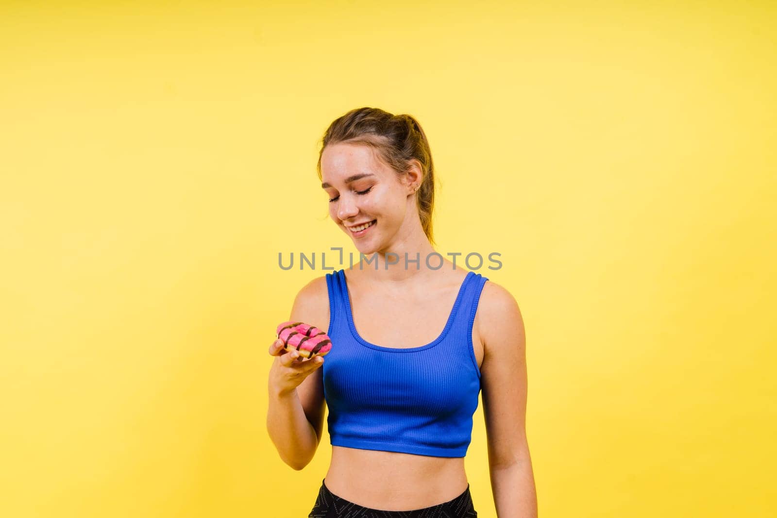Lovely young caucasian woman in sports wear with donuts on grey and yellow studio background. by Zelenin