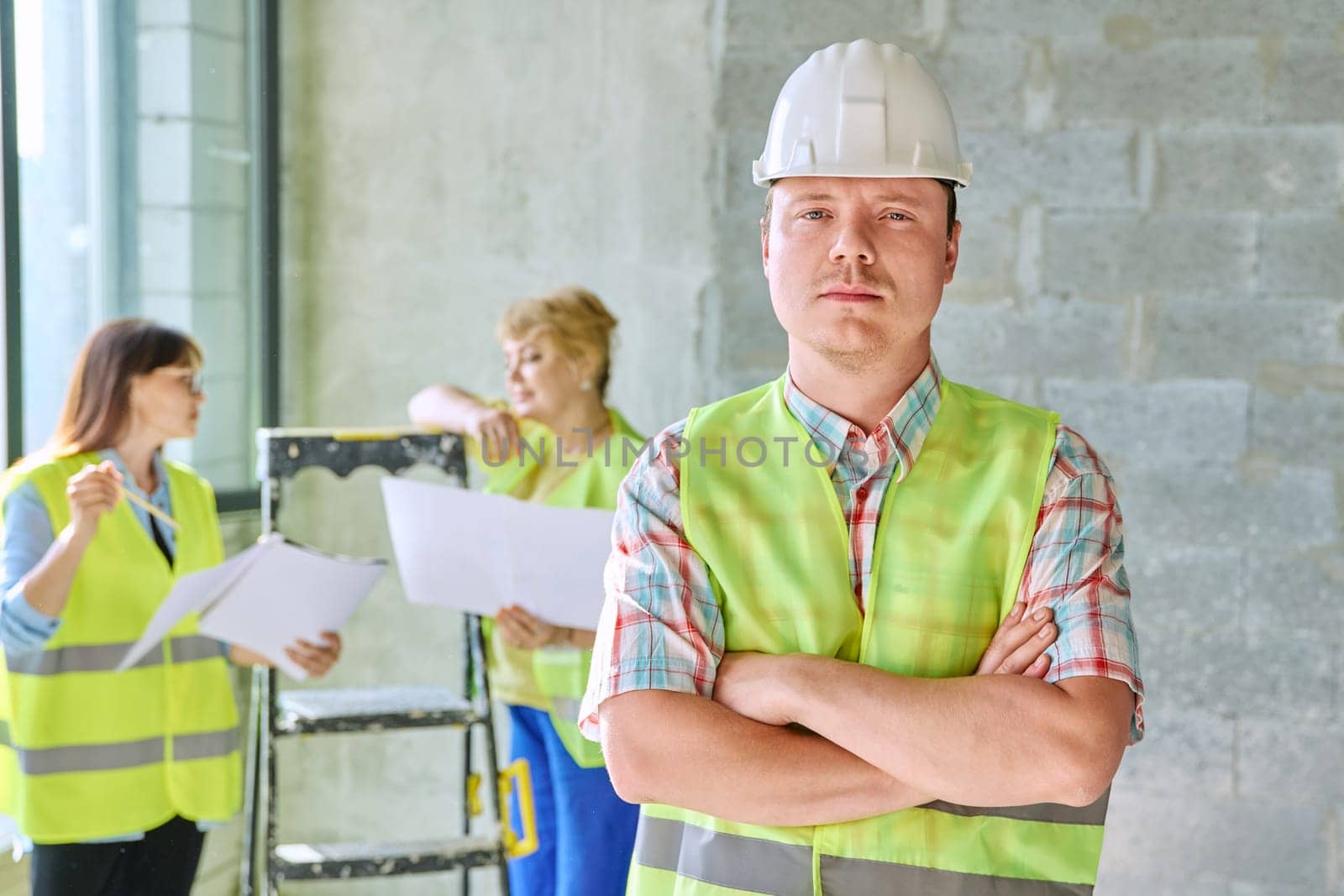 Young male industrial worker in safety helmet vest at construction site inside by VH-studio