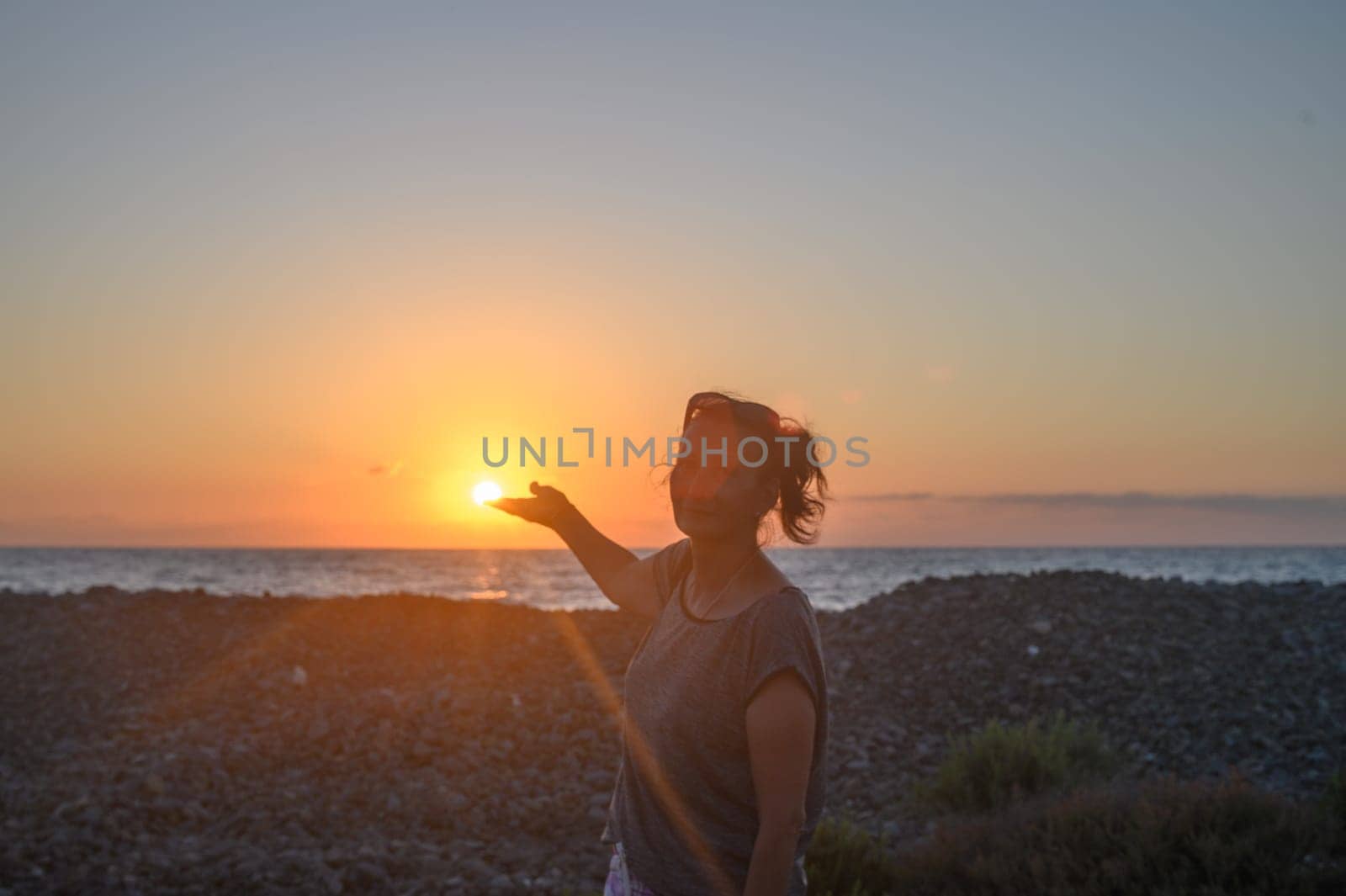 Silhouette of a young Caucasian woman holding the sun in her hands. On the seashore at sunset. 3