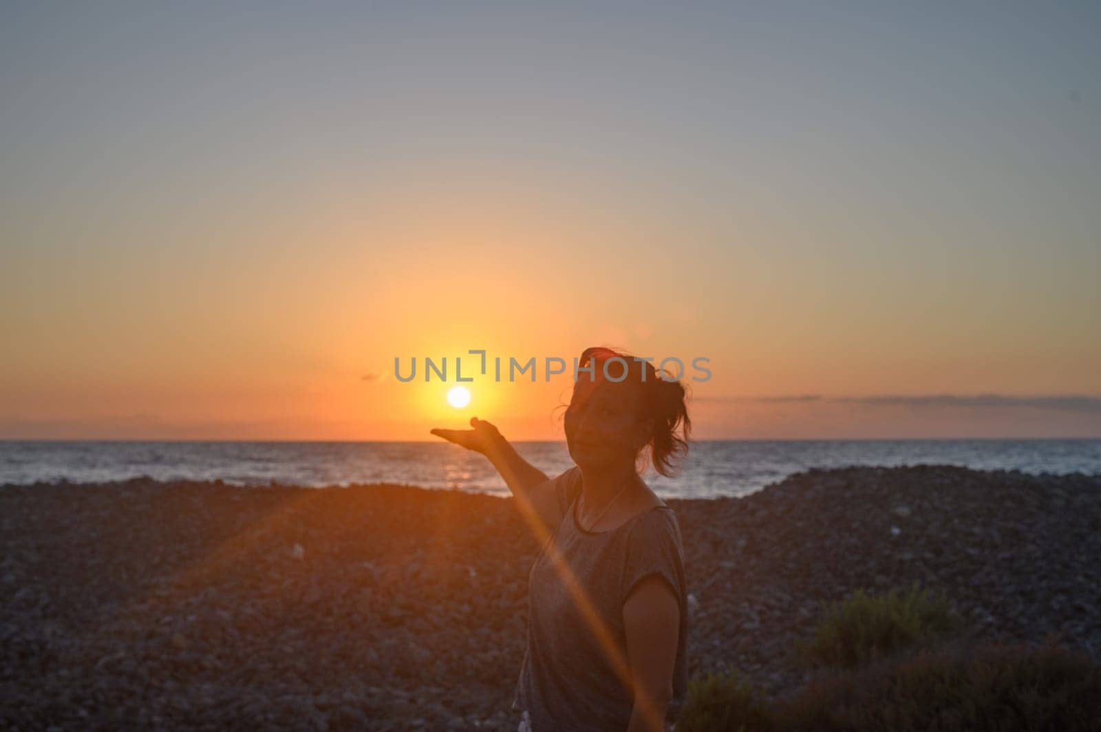 Silhouette of a young Caucasian woman holding the sun in her hands. On the seashore at sunset. 2