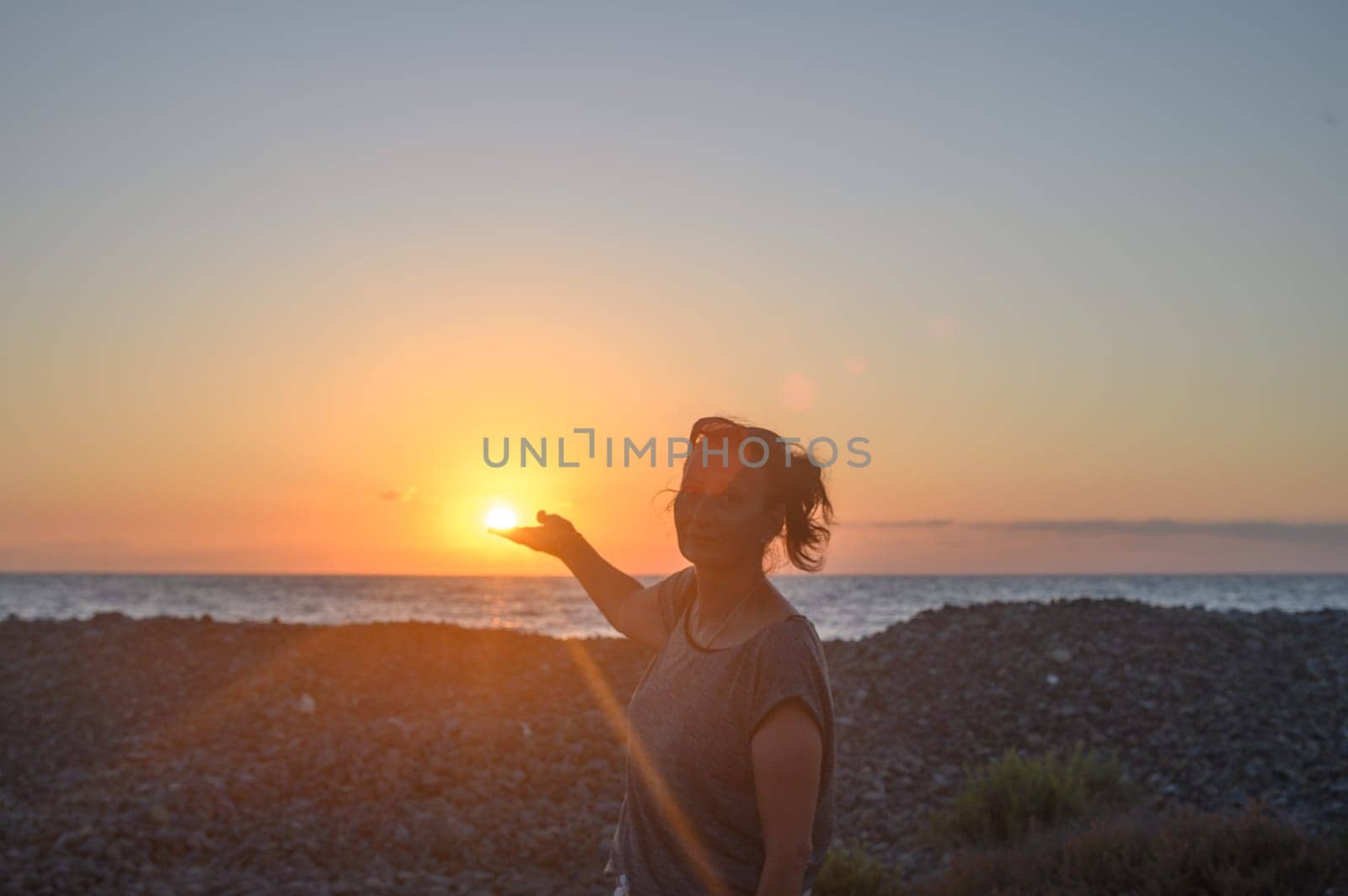 Silhouette of a young Caucasian woman holding the sun in her hands. On the seashore at sunset.1 by Mixa74
