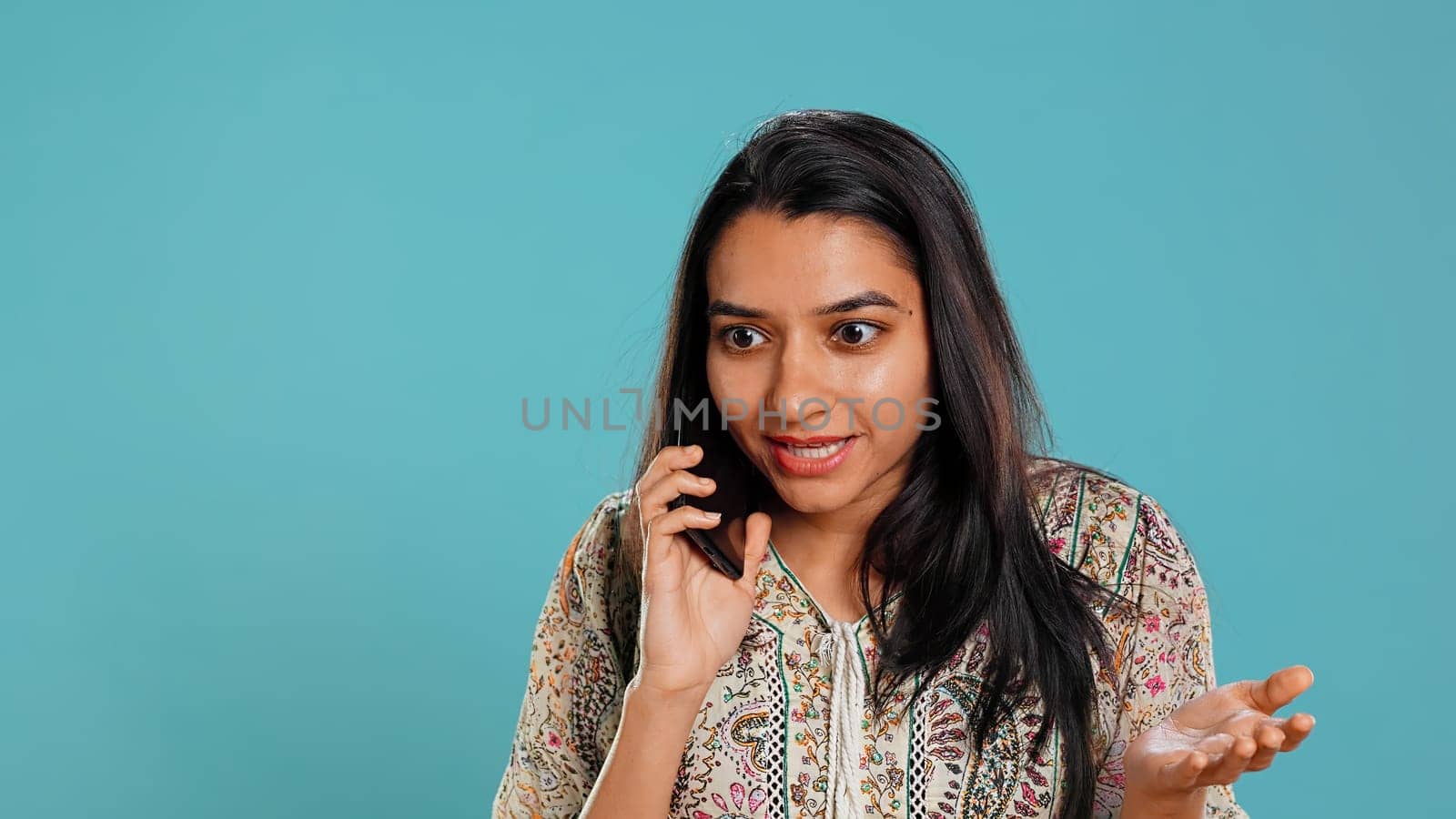 Indian woman swiping on smartphone touchscreen to answer phone call from friend, isolated over studio background. Portrait of person listening and agreeing with mate during telephone call, camera B