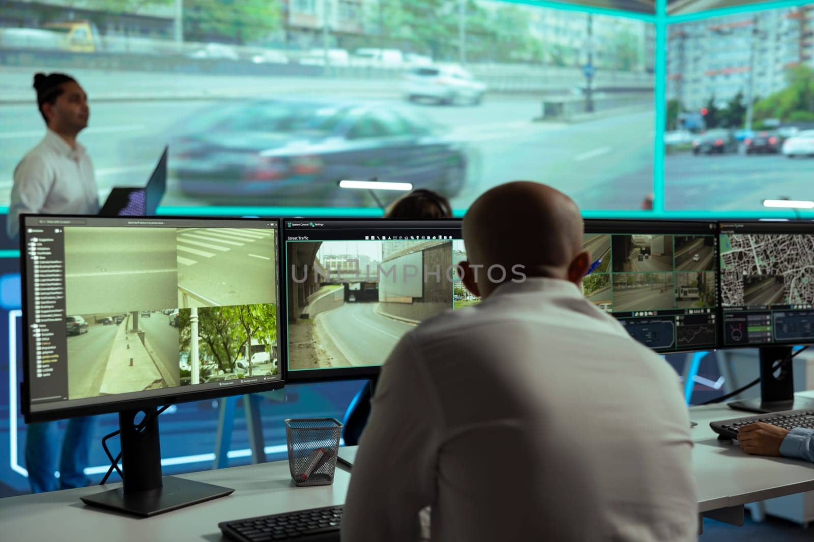 Middle eastern man overseeing the traffic surveillance footage on multiple displays, monitoring radar activity in an observation room. Team of people handling license plate reading on CCTV.