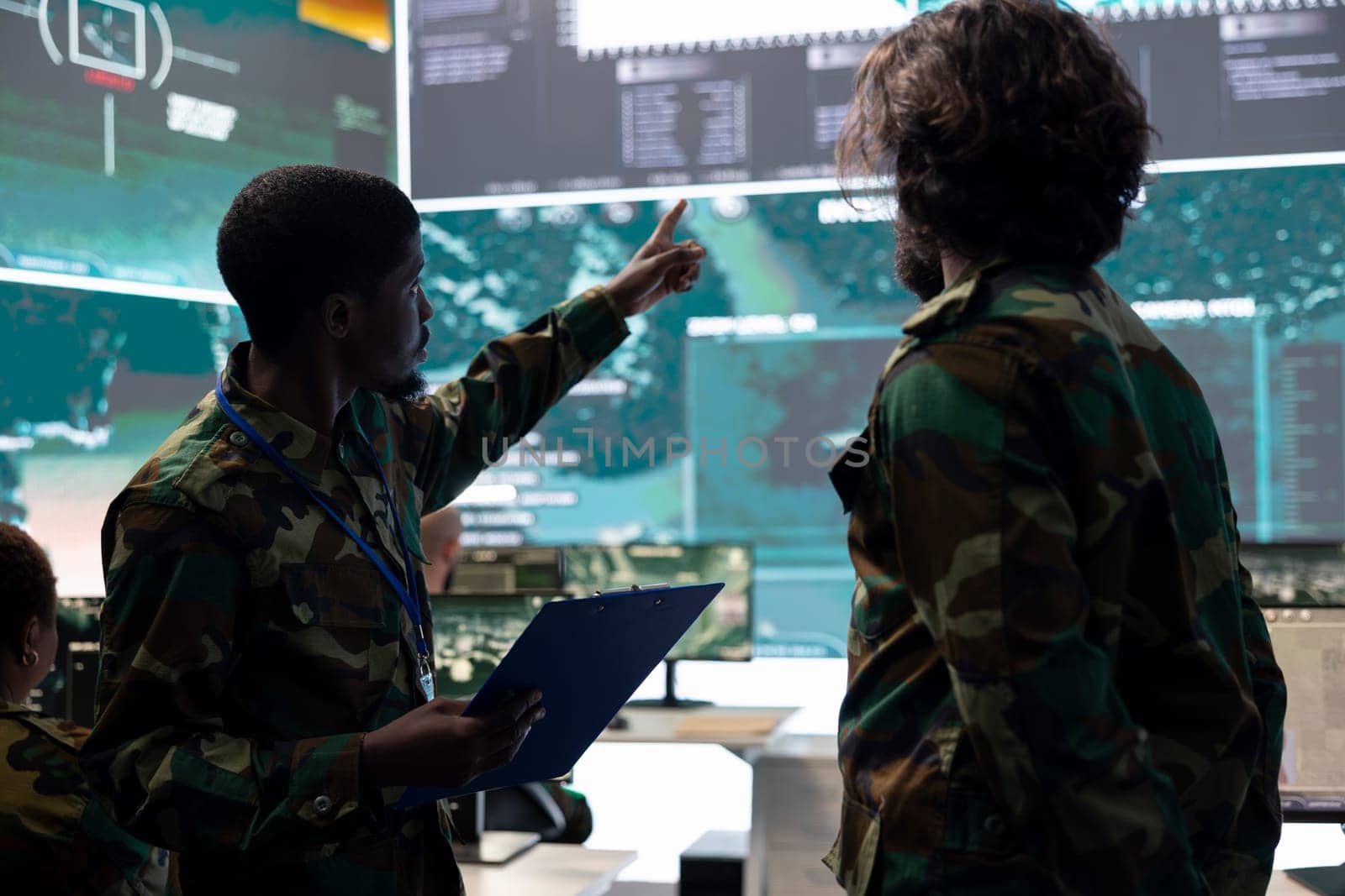 Servicemen working on new national safety plan for an operation, studying the CCTV surveillance system together in military control room. Military personnel analyze satellite support.