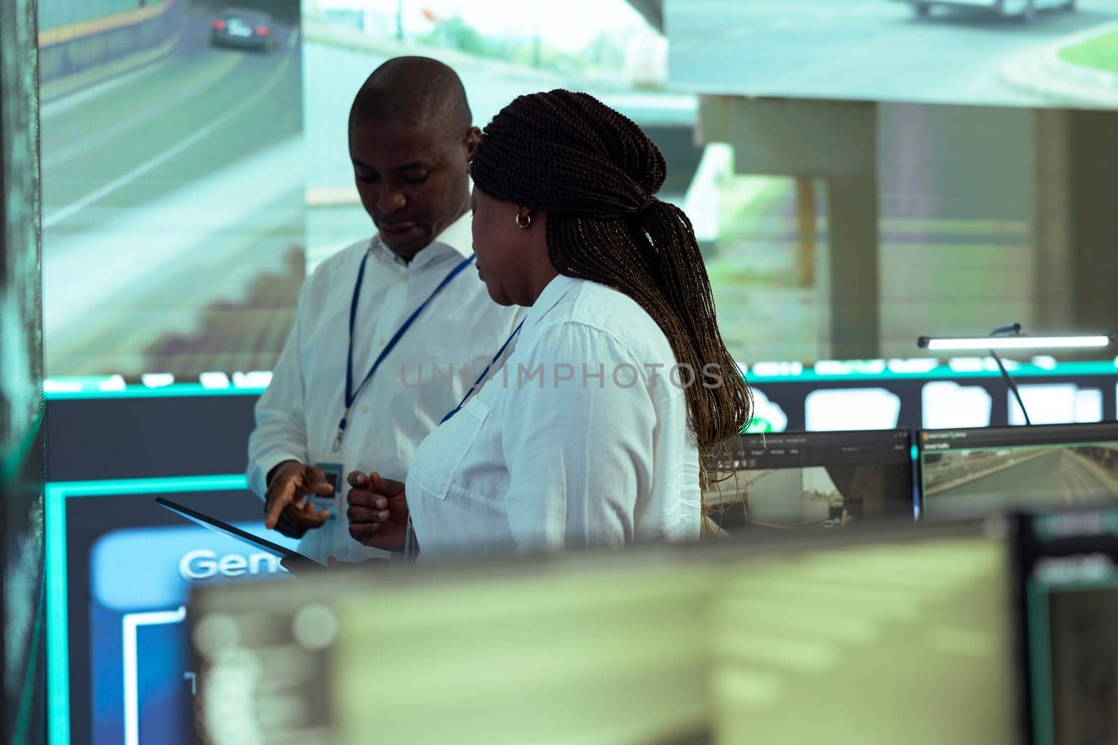 African american managers overseeing couriers activity in traffic, ensuring express delivery on alternative routes. Employees examine satellite map and CCTV city surveillance footage.