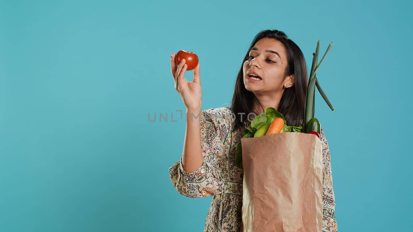 Woman with recycled paper bag in hands filled with vegetables testing quality, studio background. Sustainable living person inspecting groceries after doing purchases in shop, camera A
