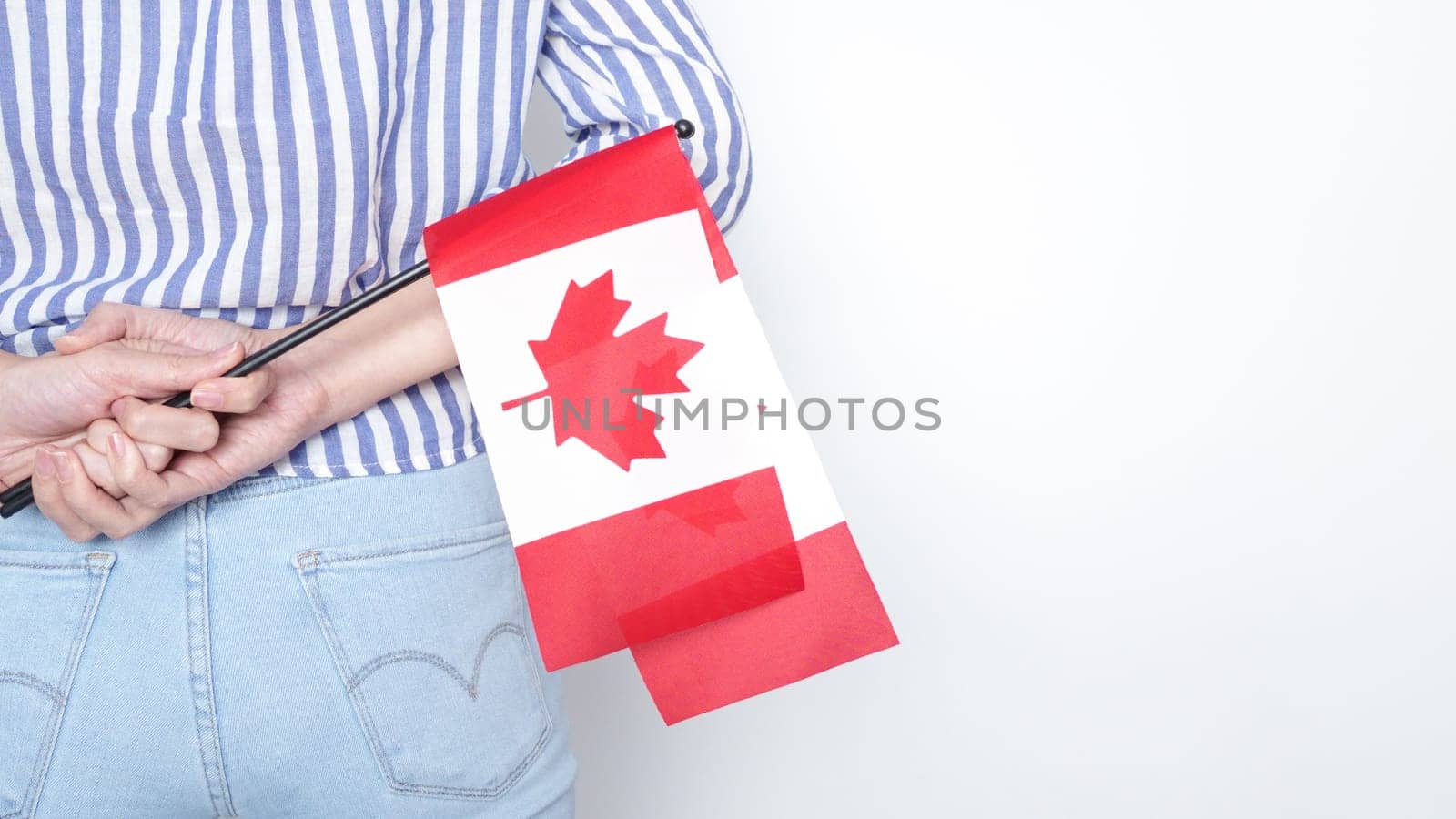 Unrecognized girl student in white blue shirt holding small Canadian flag over gray background, Canada day, holiday, vote, immigration, tax, copy space.