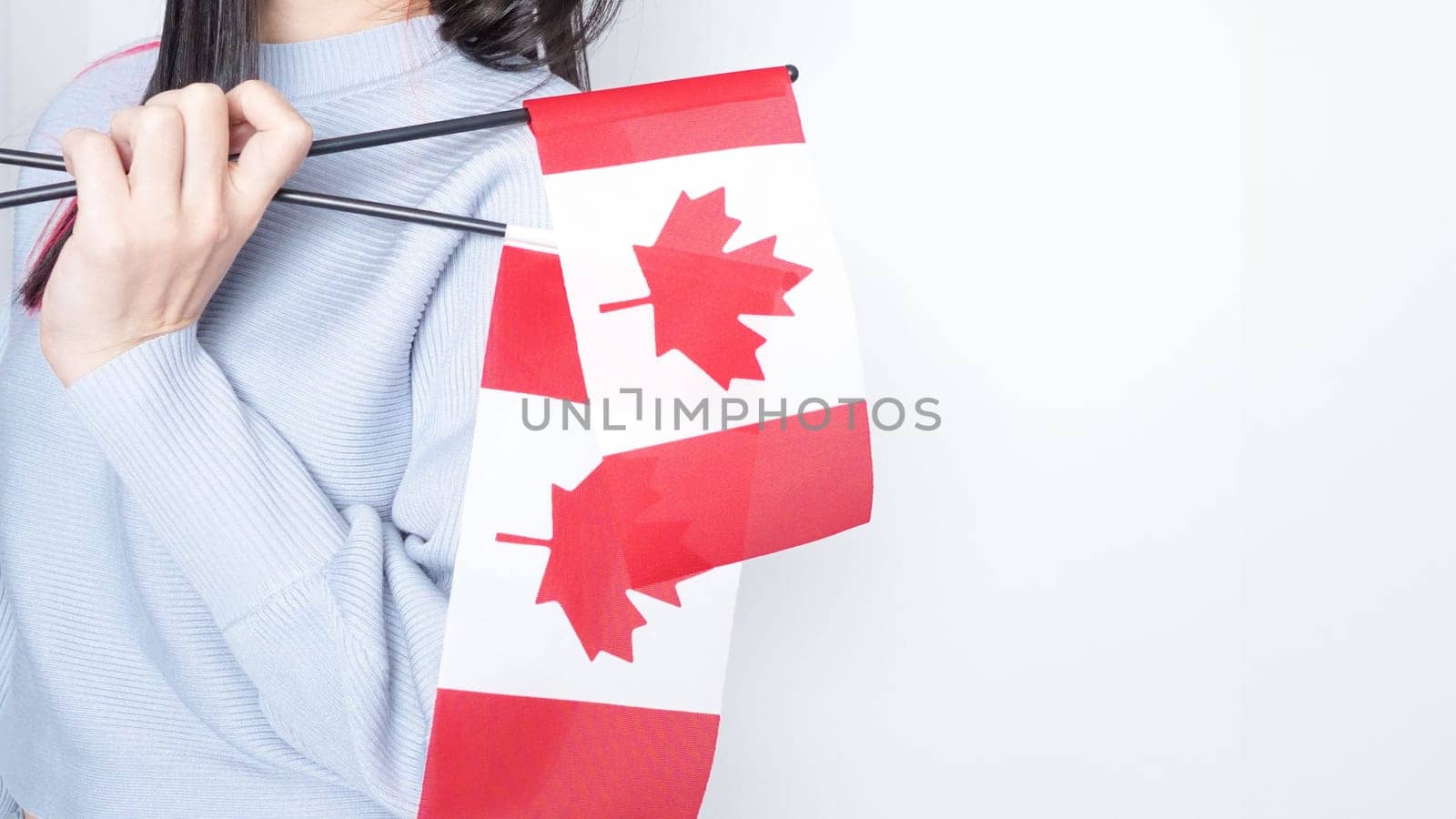 Unrecognized girl student in white blue shirt holding small Canadian flag over gray background, Canada day, holiday, vote, immigration, tax, copy space by JuliaDorian