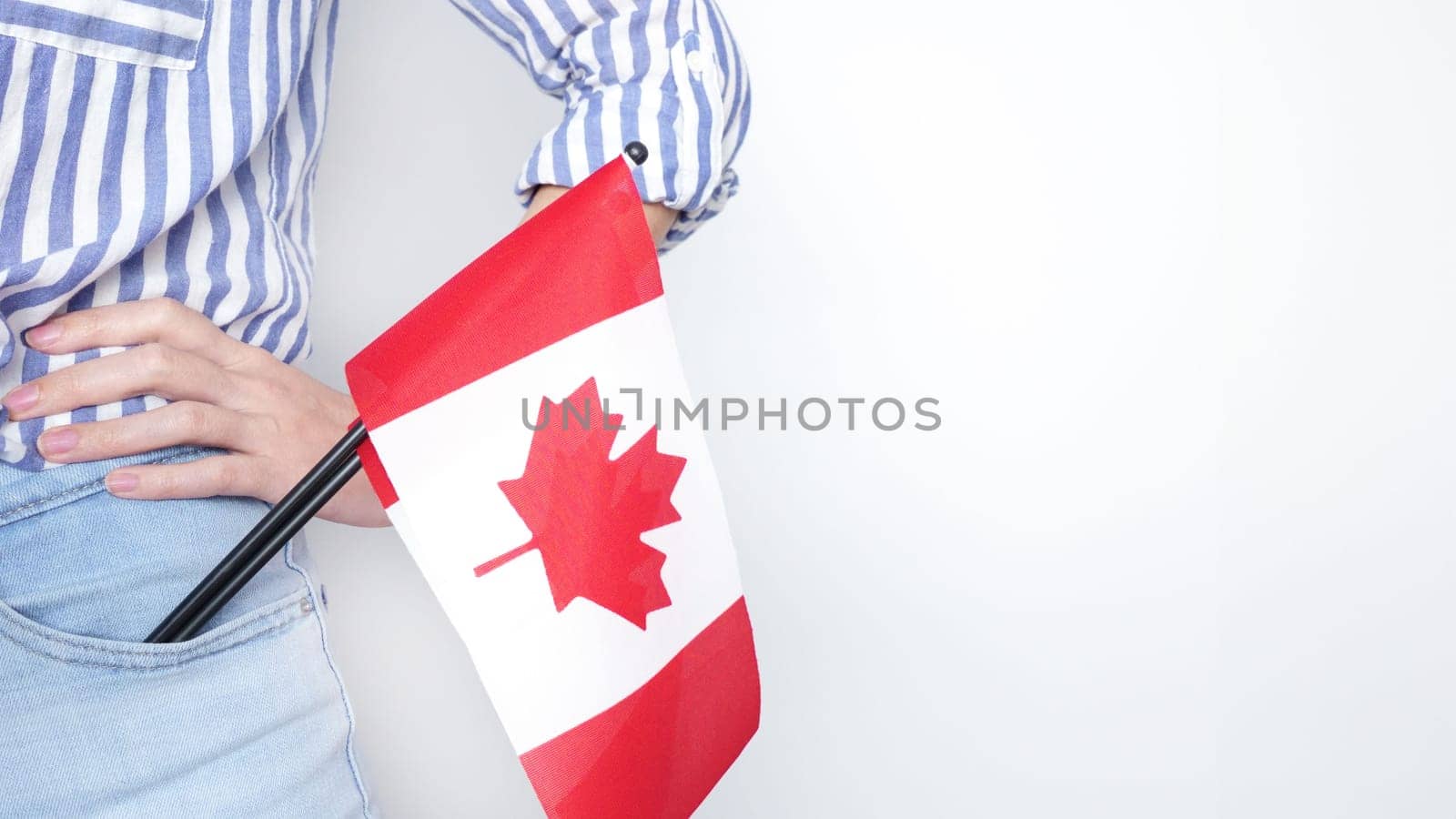 Unrecognized girl student in white blue shirt holding small Canadian flag over gray background, Canada day, holiday, vote, immigration, tax, copy space.