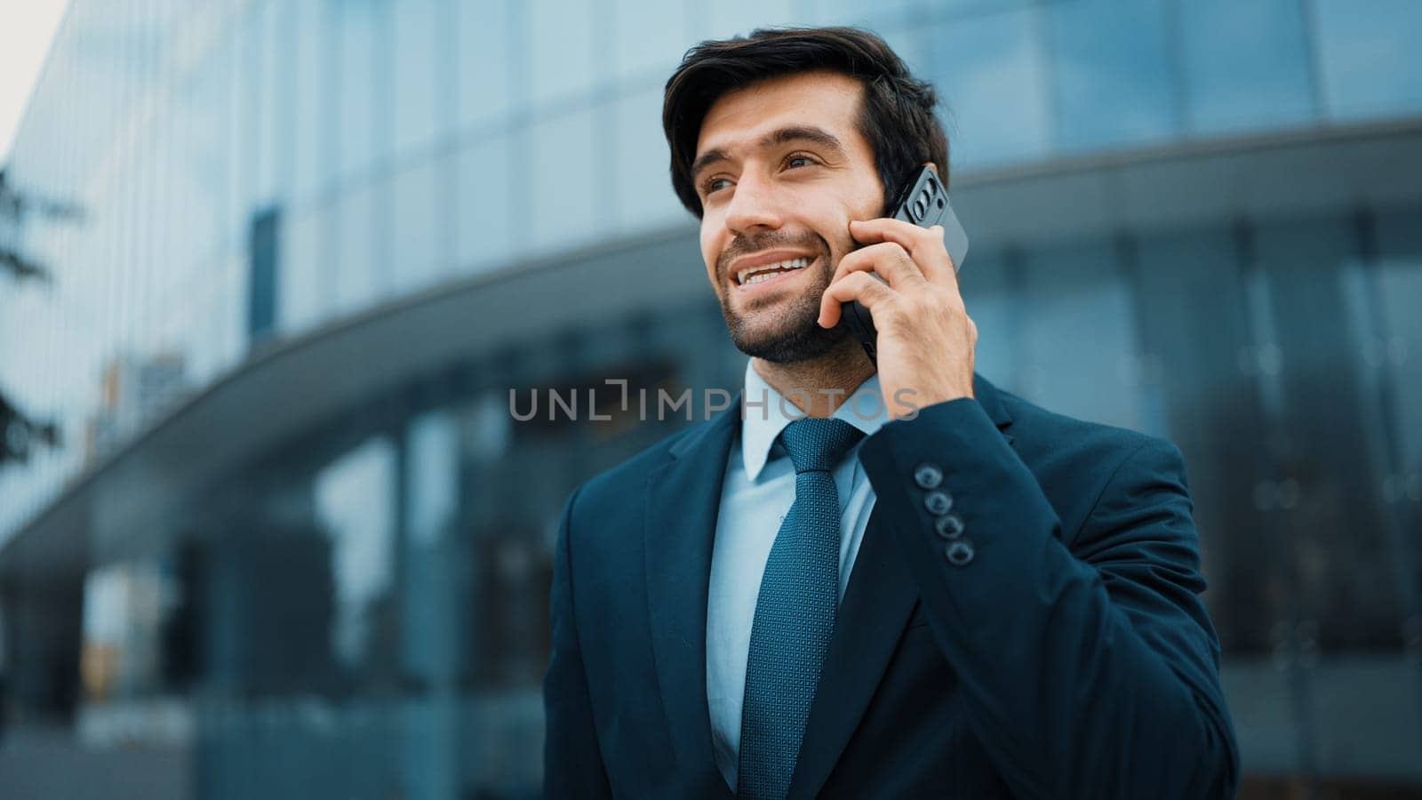 Skilled caucasian project manager calling phone while walking at city with blurred background. Skilled businessman using smart phone talking to project manager with blurred background. Exultant.