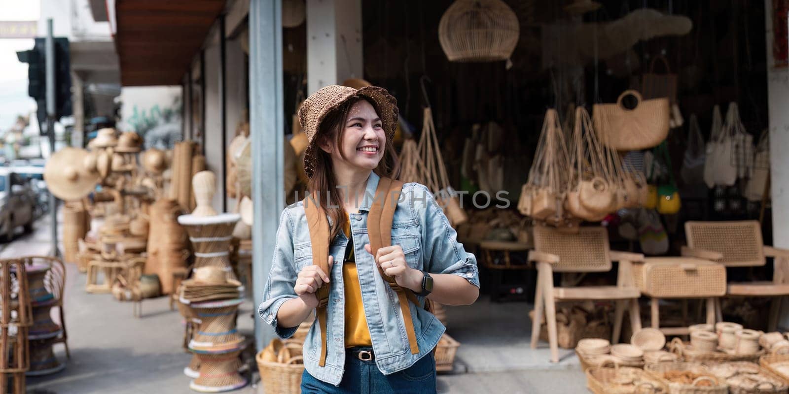 A cheerful young woman with a backpack and hat explores a local market filled with handmade crafts and souvenirs, capturing the essence of travel and adventure in an urban setting.