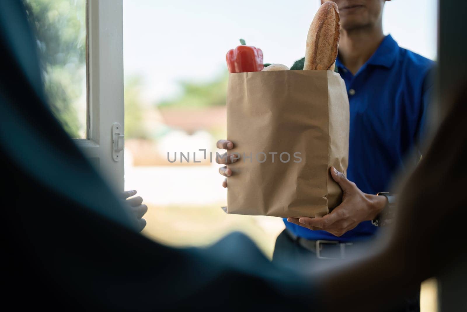 A delivery person handing over a paper bag filled with groceries at a doorstep, representing contactless delivery service during the pandemic.