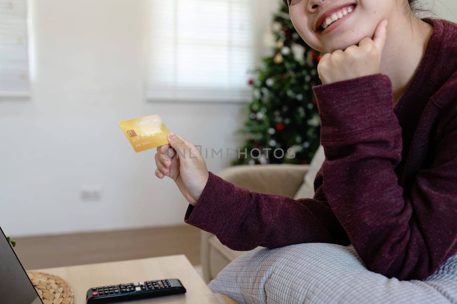 A cheerful woman holding a credit card, planning her next travel adventure from the comfort of her home, with a laptop