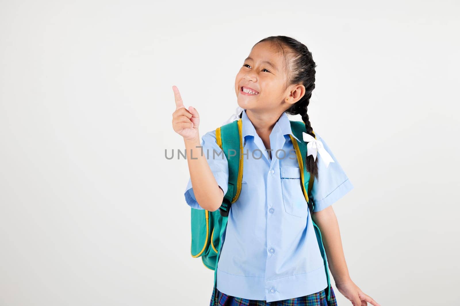 Portrait smiling Asian little girl kindergarten with schoolbag pointing finger at copy space studio shot isolated white background, happy woman kid in pigtails wearing school uniform, back to school